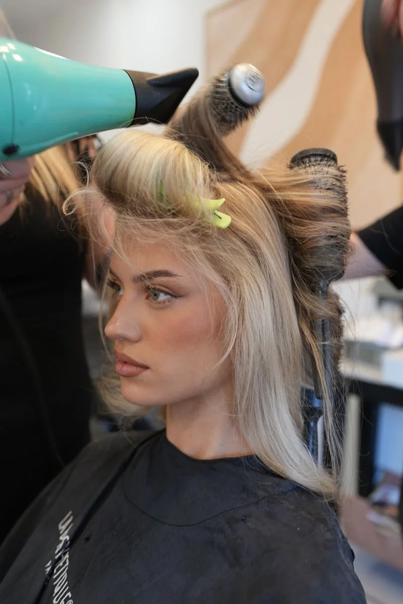A woman is getting her hair blow-dried and styled with rollers in her hair at a salon.