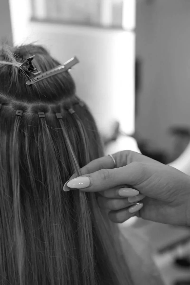 A person getting hair extensions or weaves attached to their hair by a hairstylist in a salon.