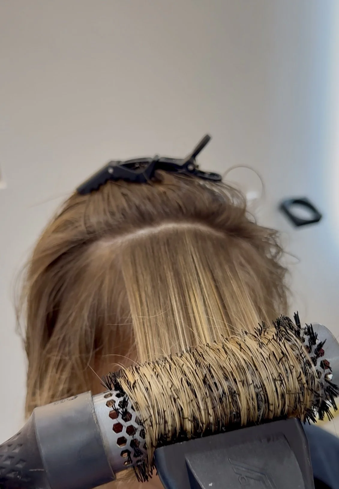 Hairdresser using a round brush and a blow dryer to style a person's blonde hair.