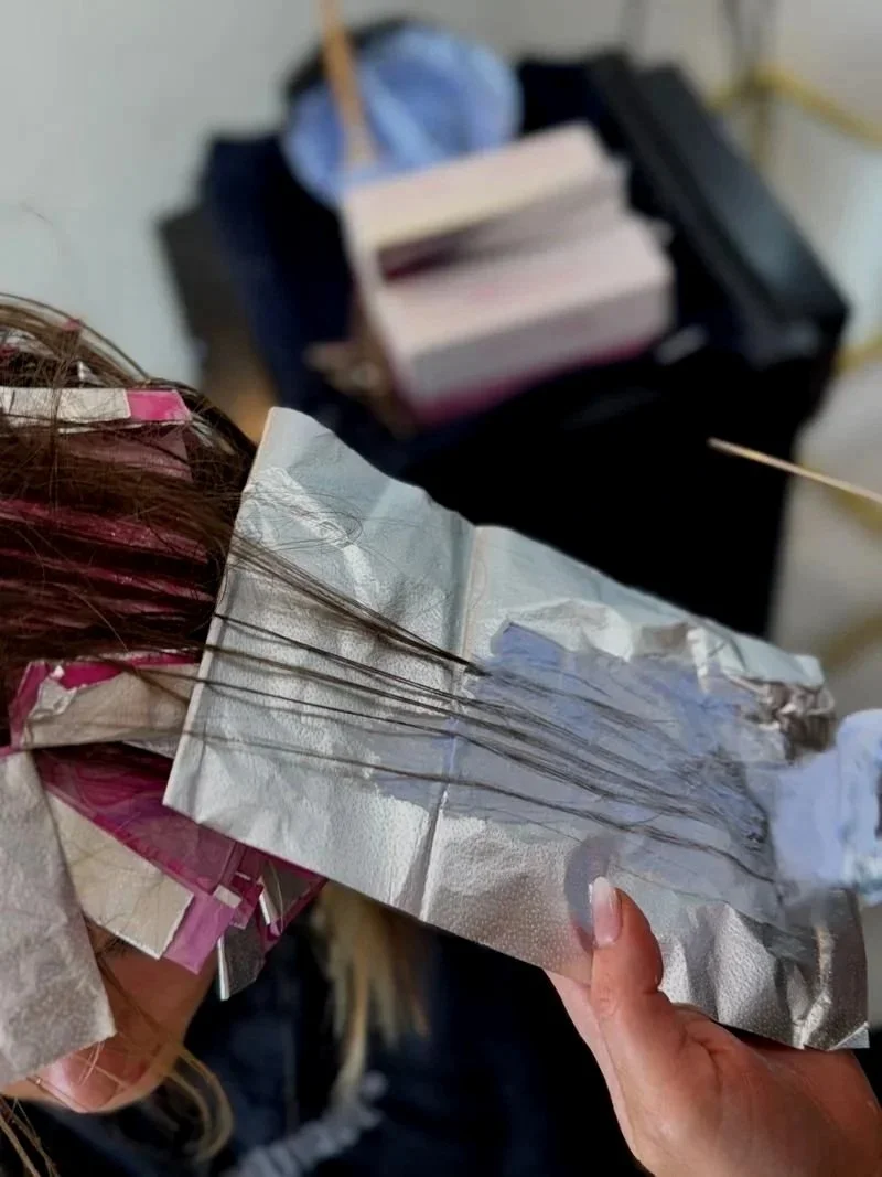 Someone holding a strip of aluminum foil with thin, dark hair strands attached to it, hair coloring or highlighting process in progress.