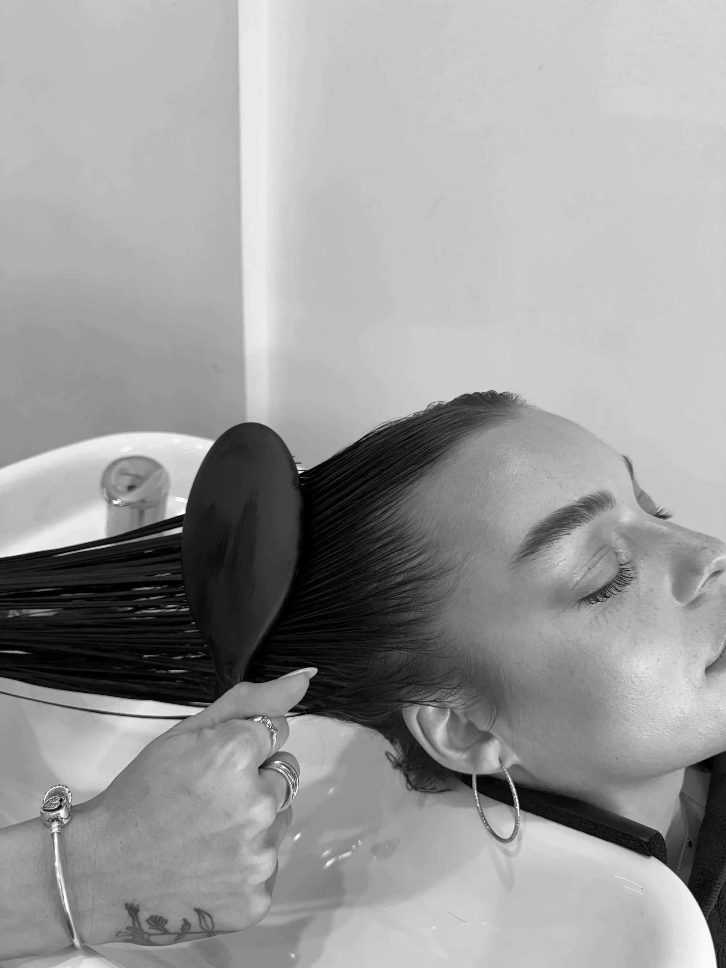 Shó Hair Studio client leaning back in a salon sink, getting her hair washed by a stylist with a large paddle brush.
