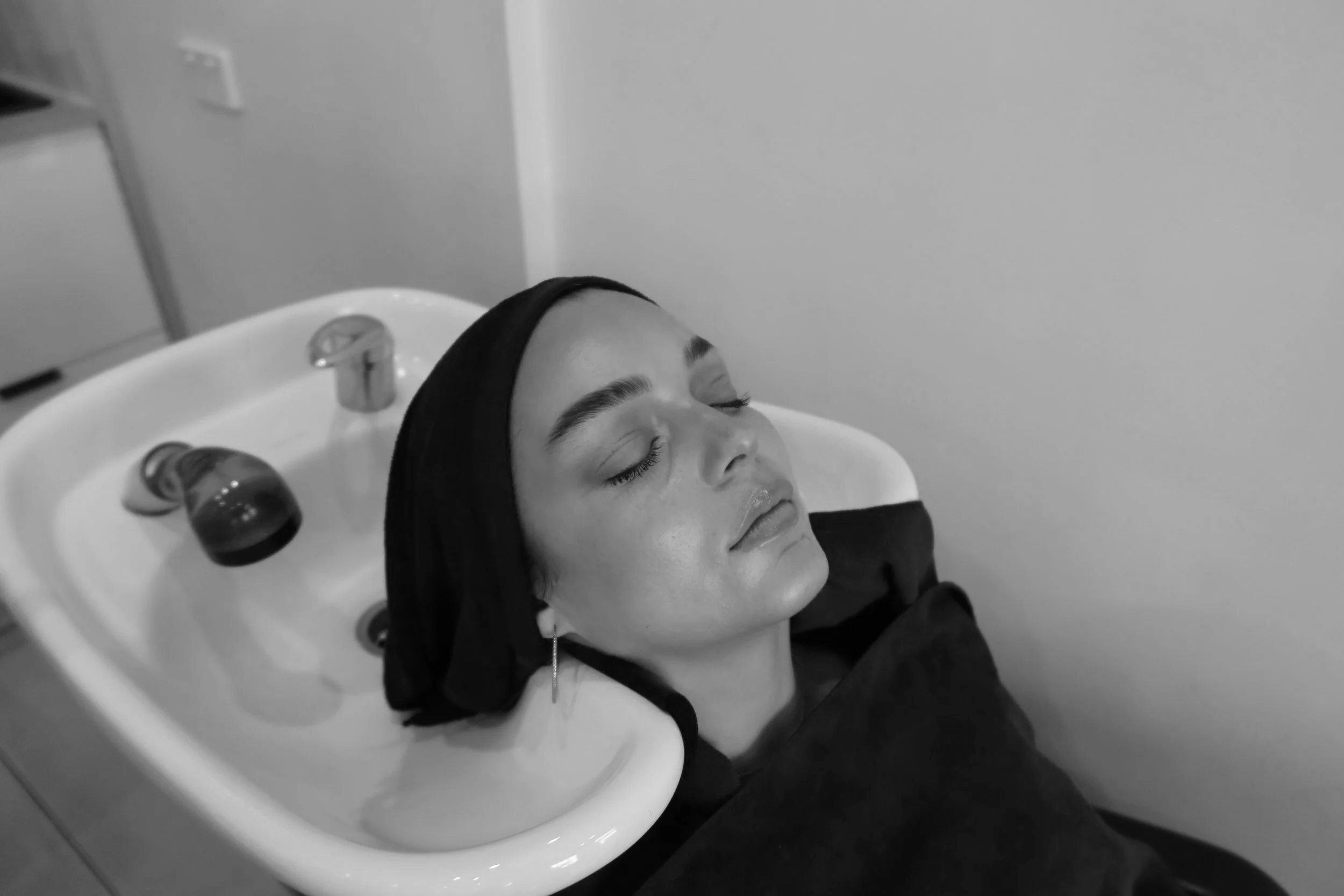Woman with closed eyes receiving hair treatment at salon, head resting in sink