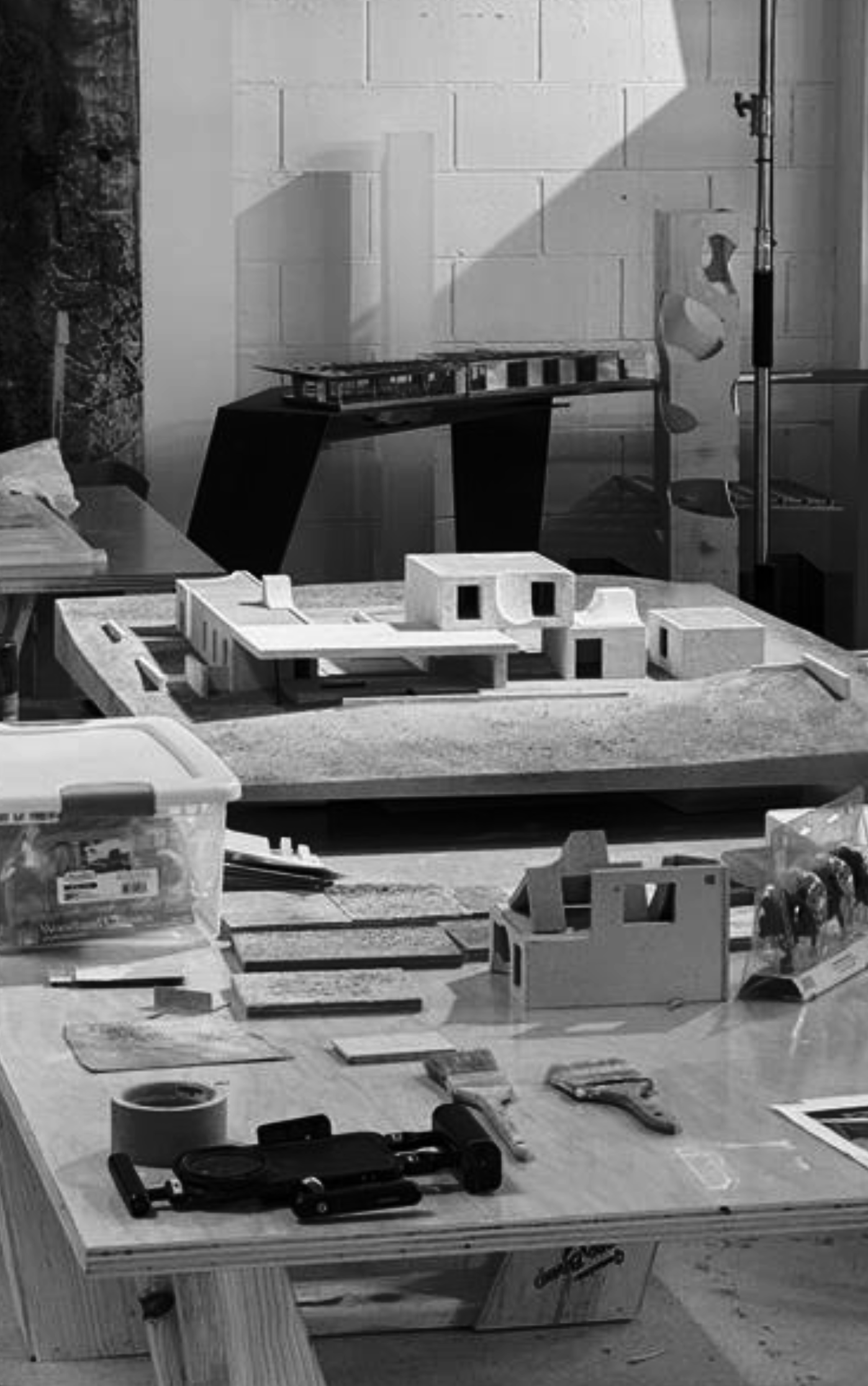A workspace with architectural models, tools, and supplies on a wooden table, with finished models and materials for building models.