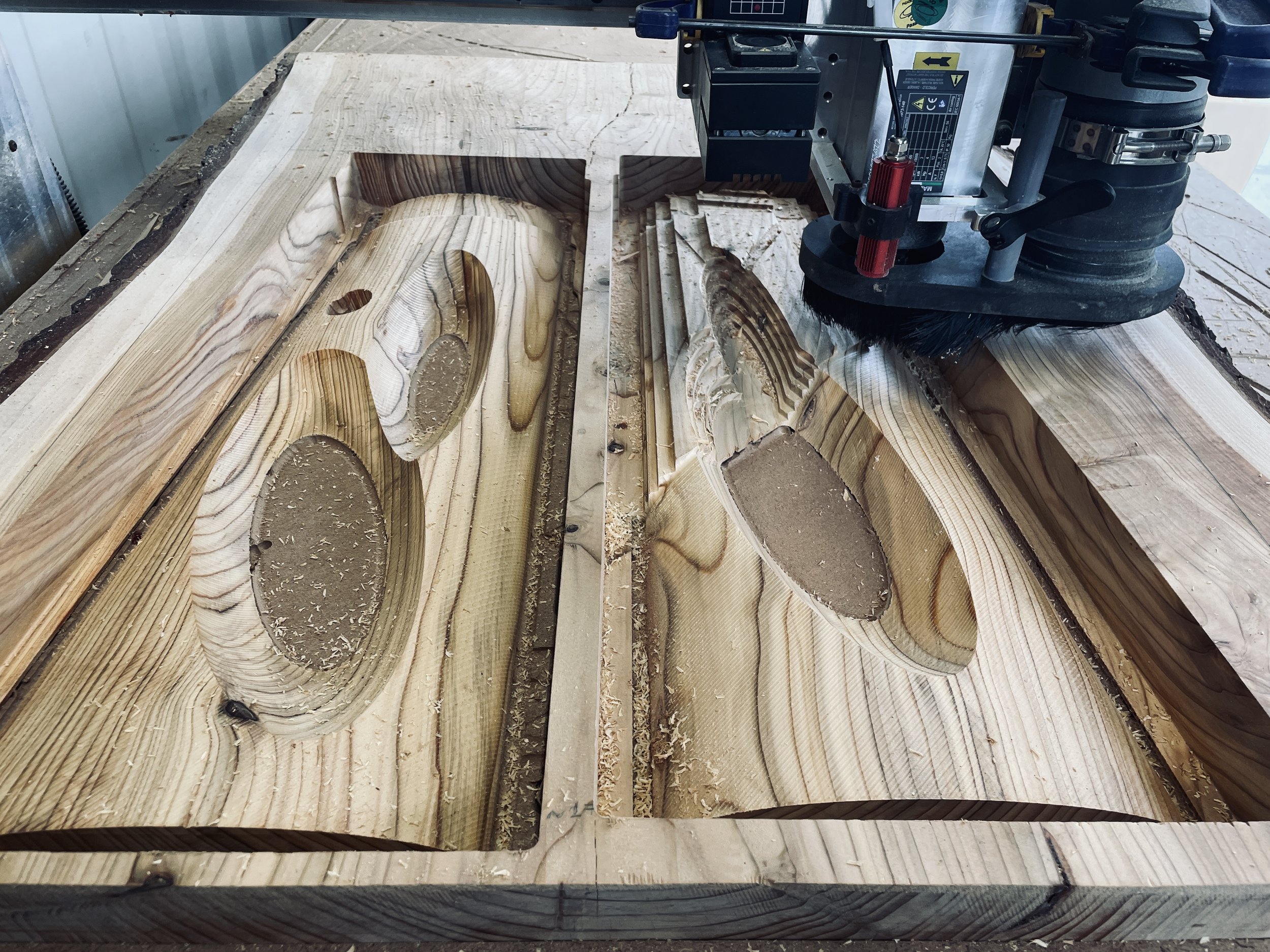 A cnc router machine shaping a large piece of wood with oval holes.