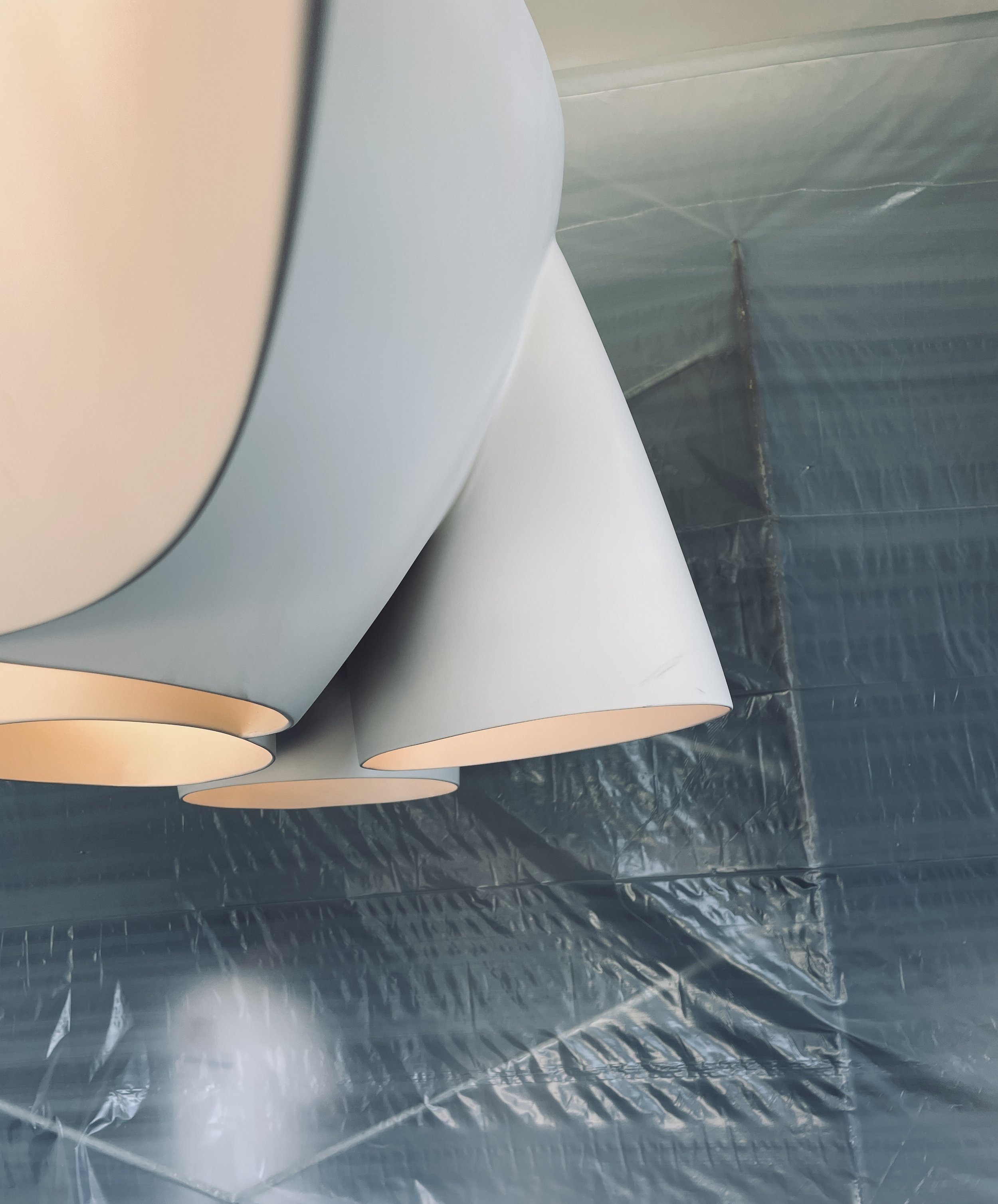Close-up view of modern, cone-shaped white pendant lights hanging from the ceiling, against a reflective, textured ceiling surface.