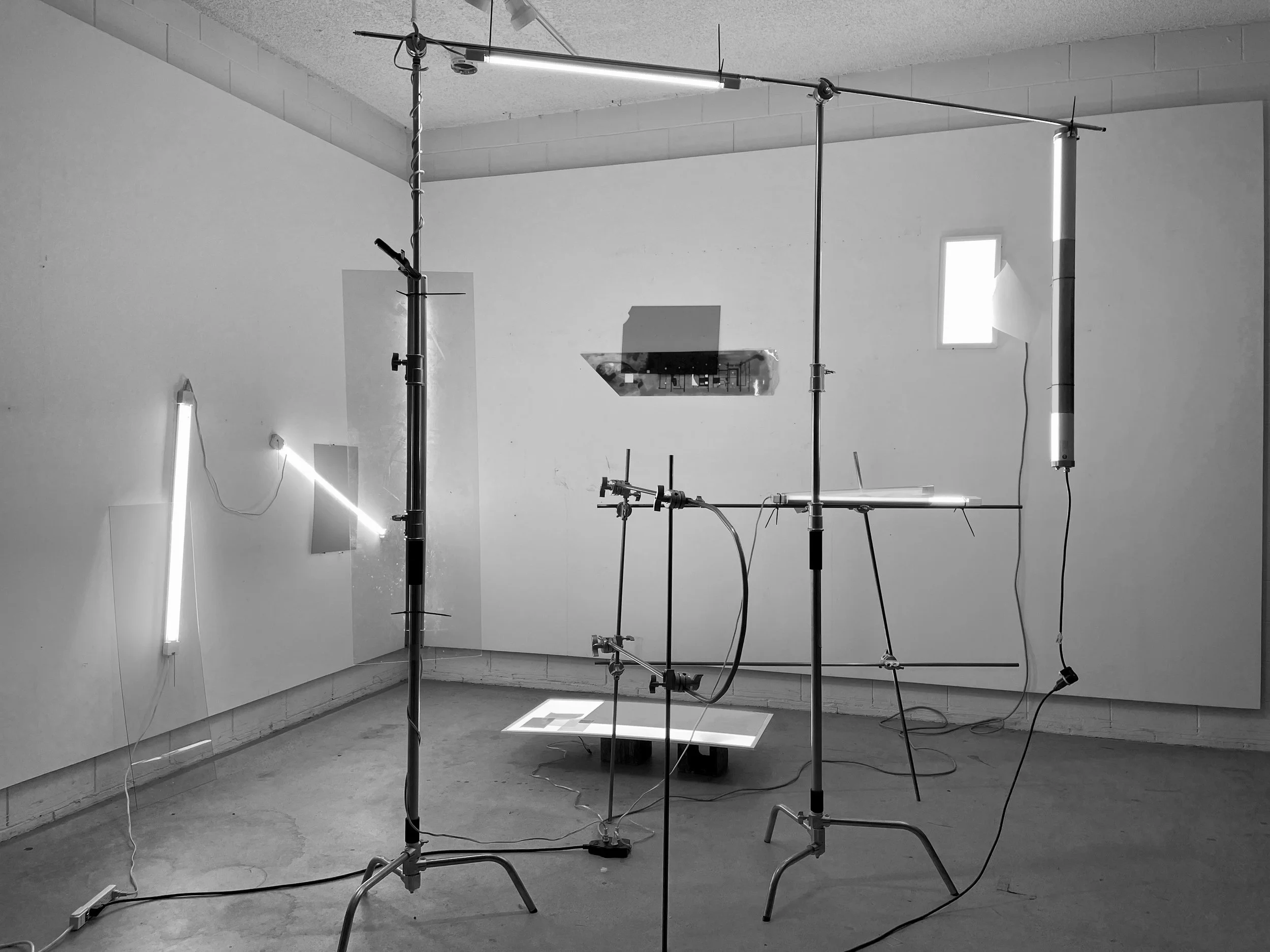An art installation featuring vertical and horizontal metal poles with attached light fixtures and wires in a gallery space.