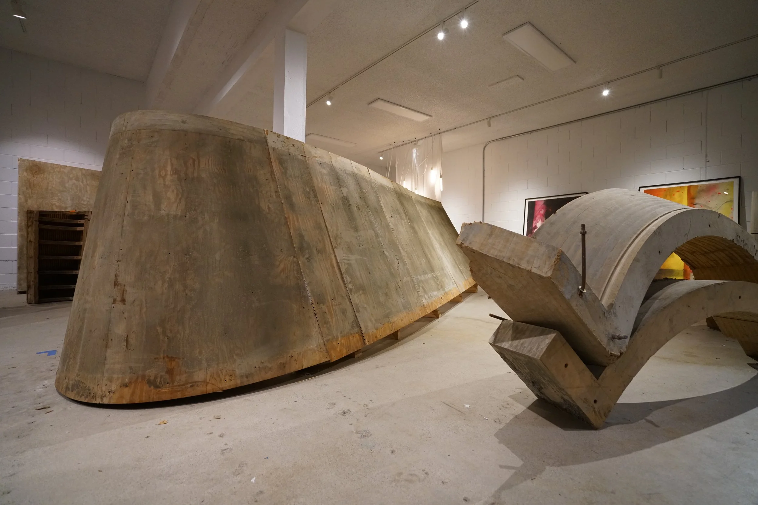 Large abstract sculptures made of cnc milled billet wood in an art gallery, with paintings on the wall in the background.