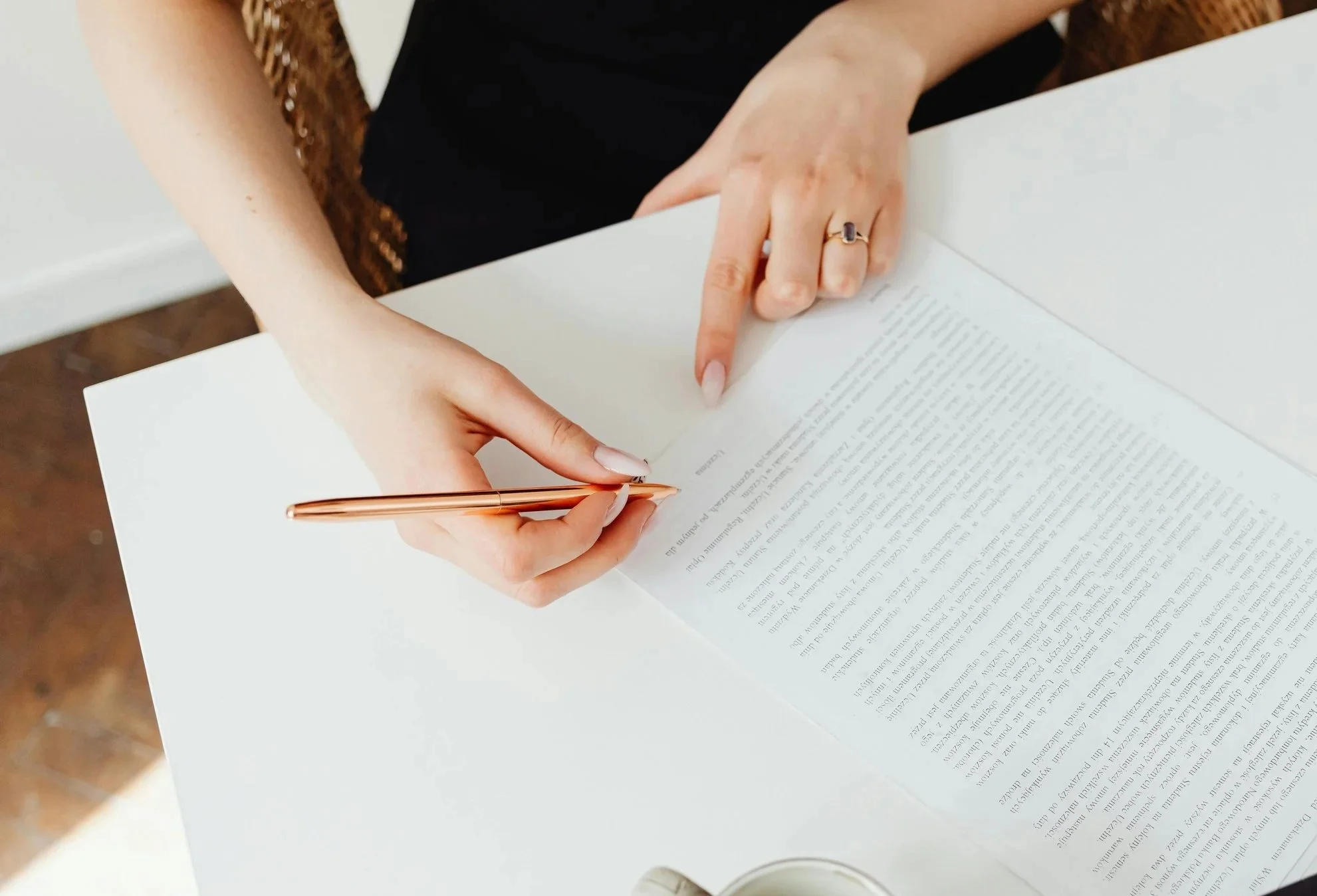 Eine Person schreibt mit einem rosafarbenen Kugelschreiber auf einem Dokument auf einem weißen Tisch.