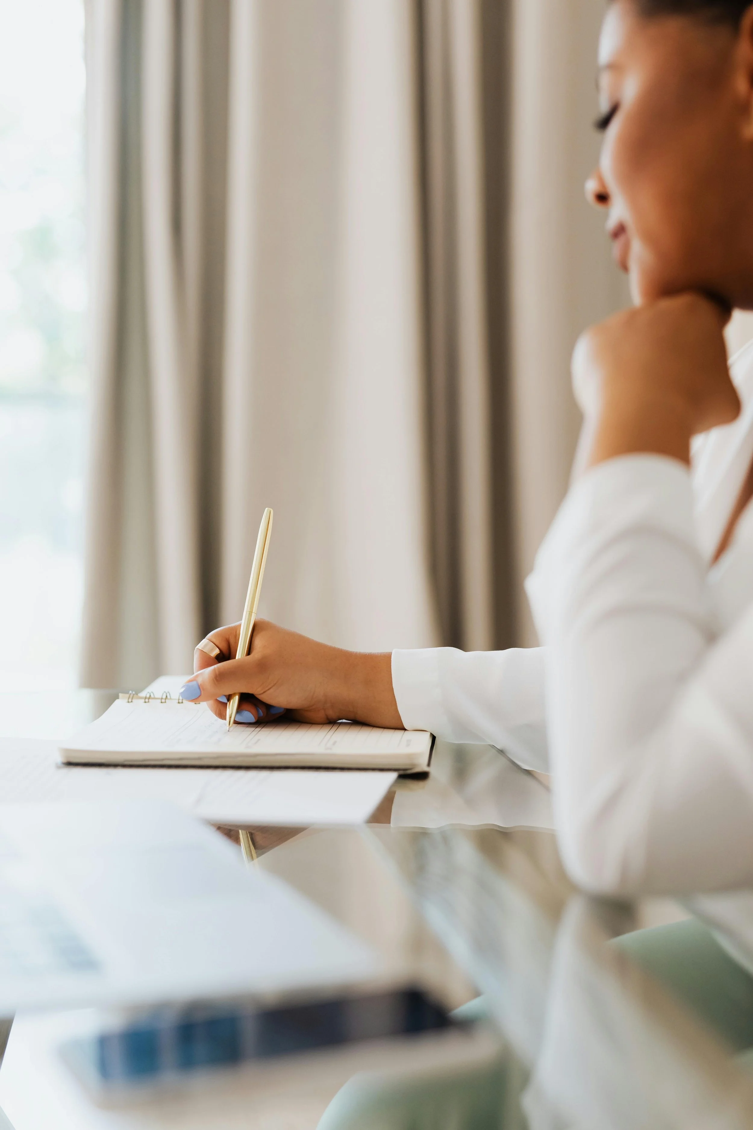 Frau schreibt in ein Notizbuch, während sie in einem hell erleuchteten Raum sitzt.