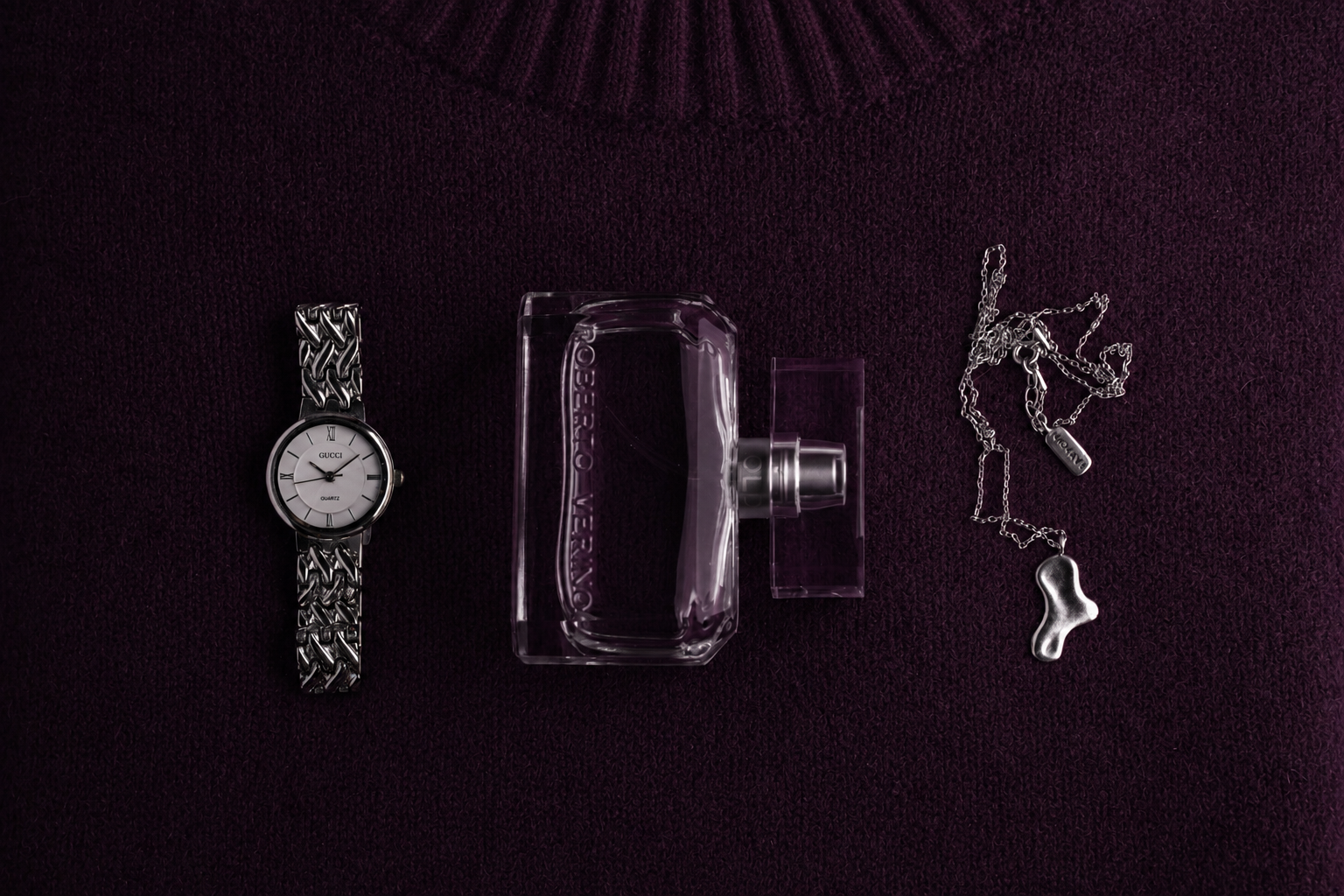 Eine Gucci-Armbanduhr, eine Flasche Parfüm, eine silberne Halskette mit Anhänger auf lila Stoff