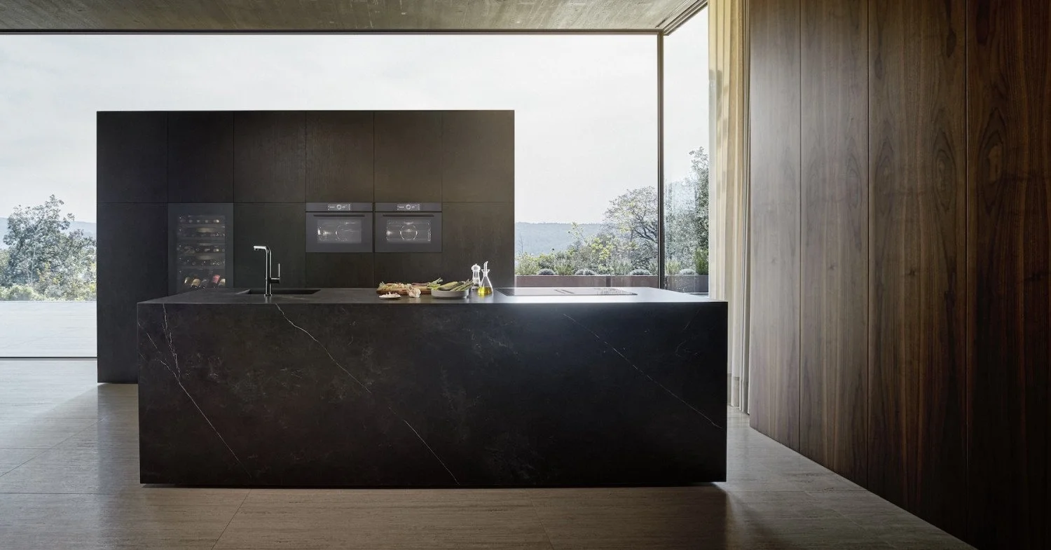 Modern kitchen with a black marble island and wall cabinets, large window with scenic view, and built-in appliances.