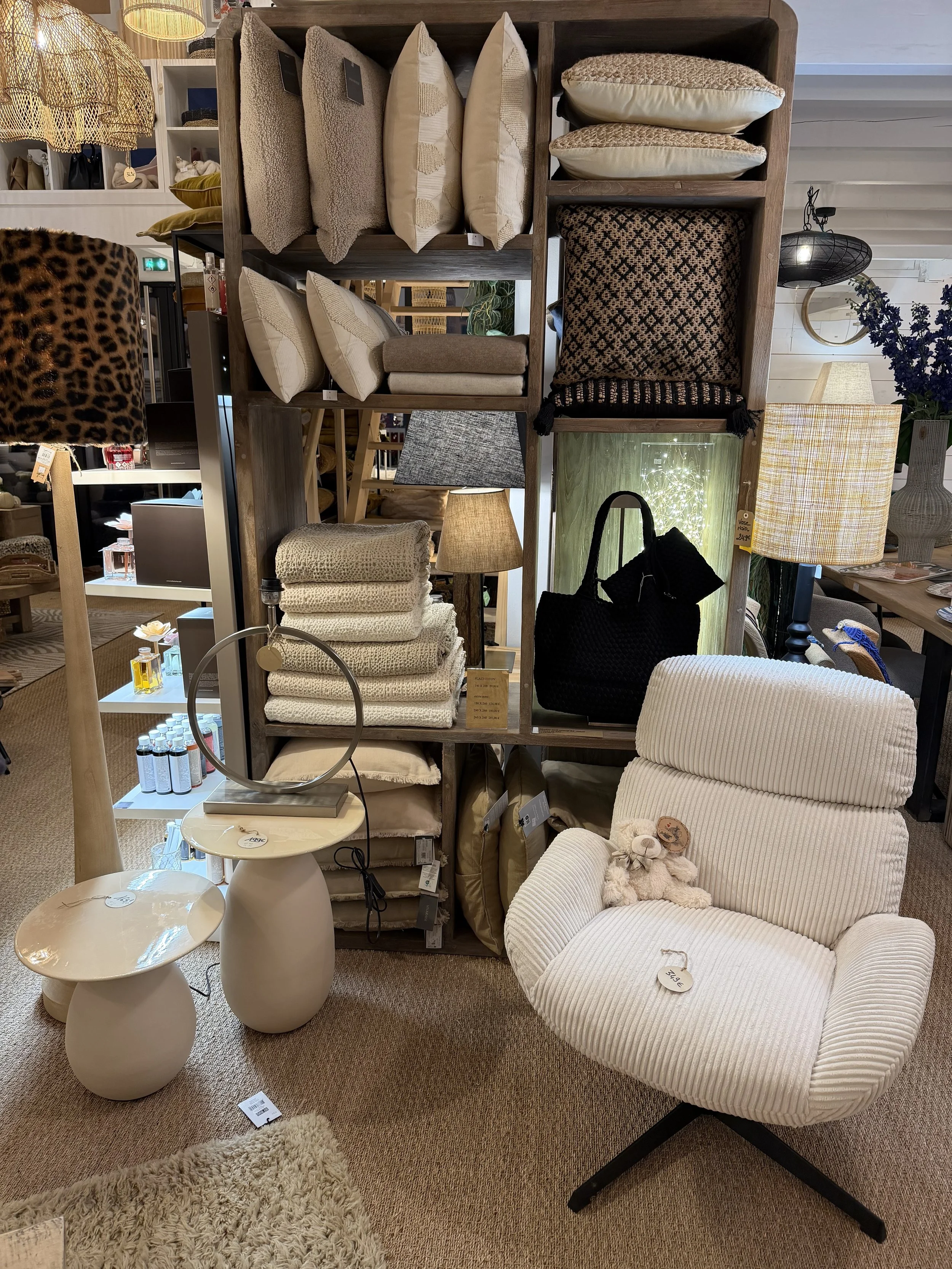 Une pièce d'ameublement avec des coussins, des lampes, un fauteuil beige rayé, et deux petites tables blanches dans un magasin de décoration intérieure.