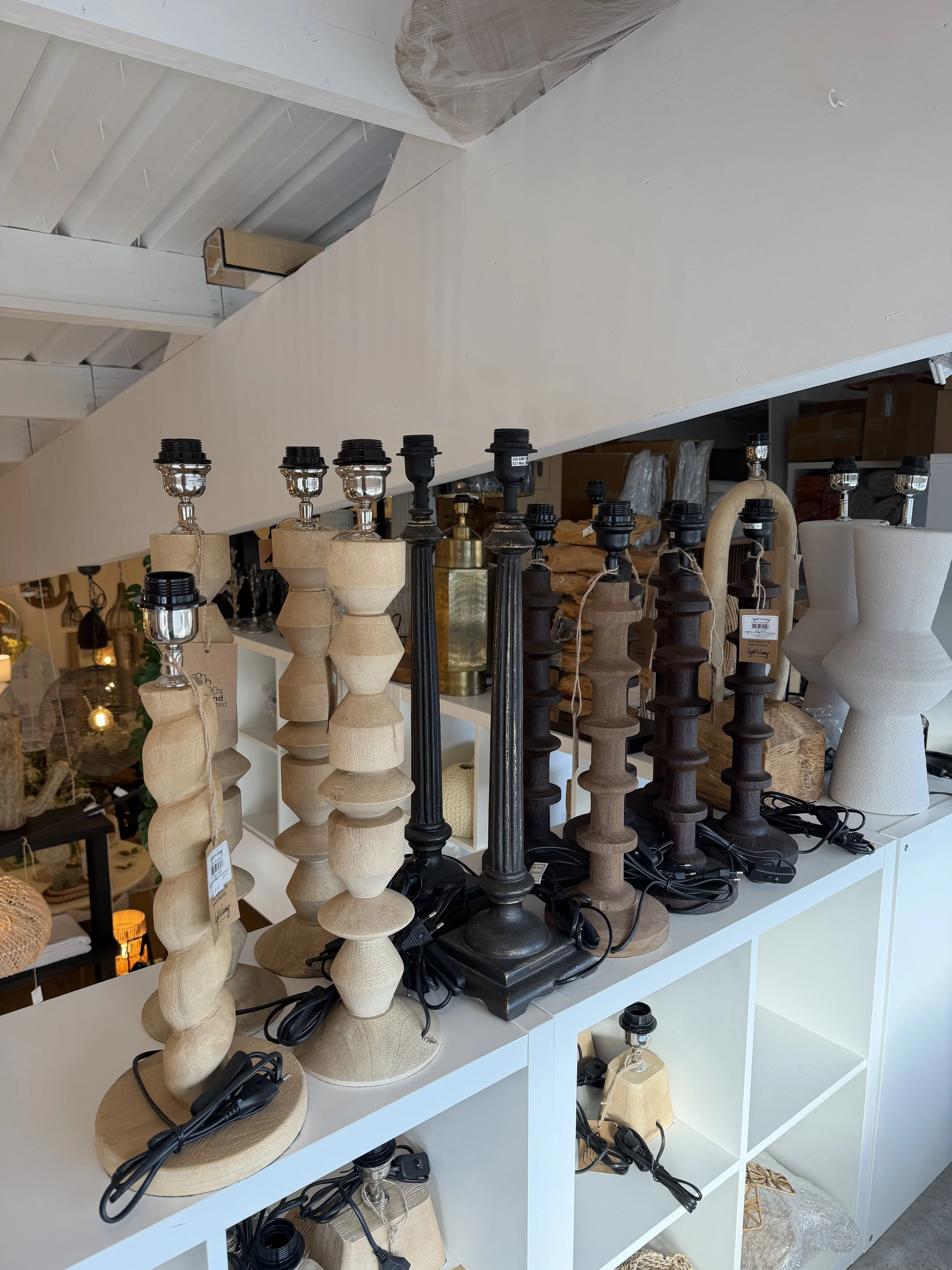 Une variété de lampes de table en bois de différentes couleurs et formes exposées sur une étagère dans un magasin d'ameublement.