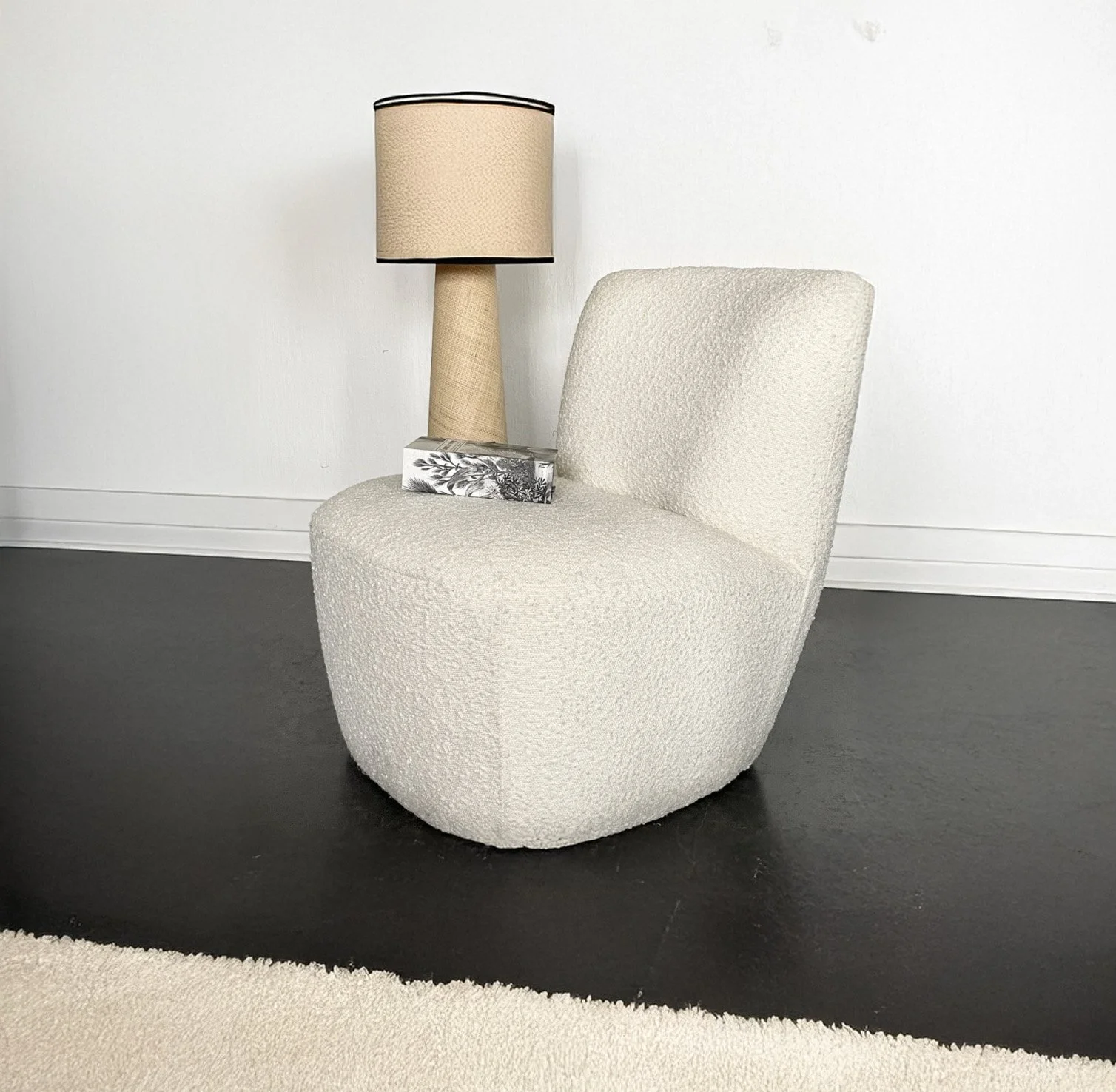 Fauteuil beige avec lampe de table et boîte de mouchoirs sur le siège, mur blanc en fond, sol noir et tapis blanc à gauche.