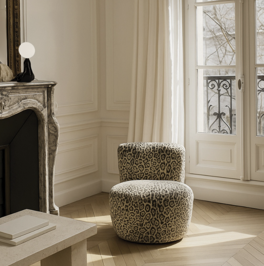 Intérieur d'une pièce lumineuse avec une chaise à motif léopard, une cheminée en marbre et une fenêtre donnant sur un balcon en fer forgé.