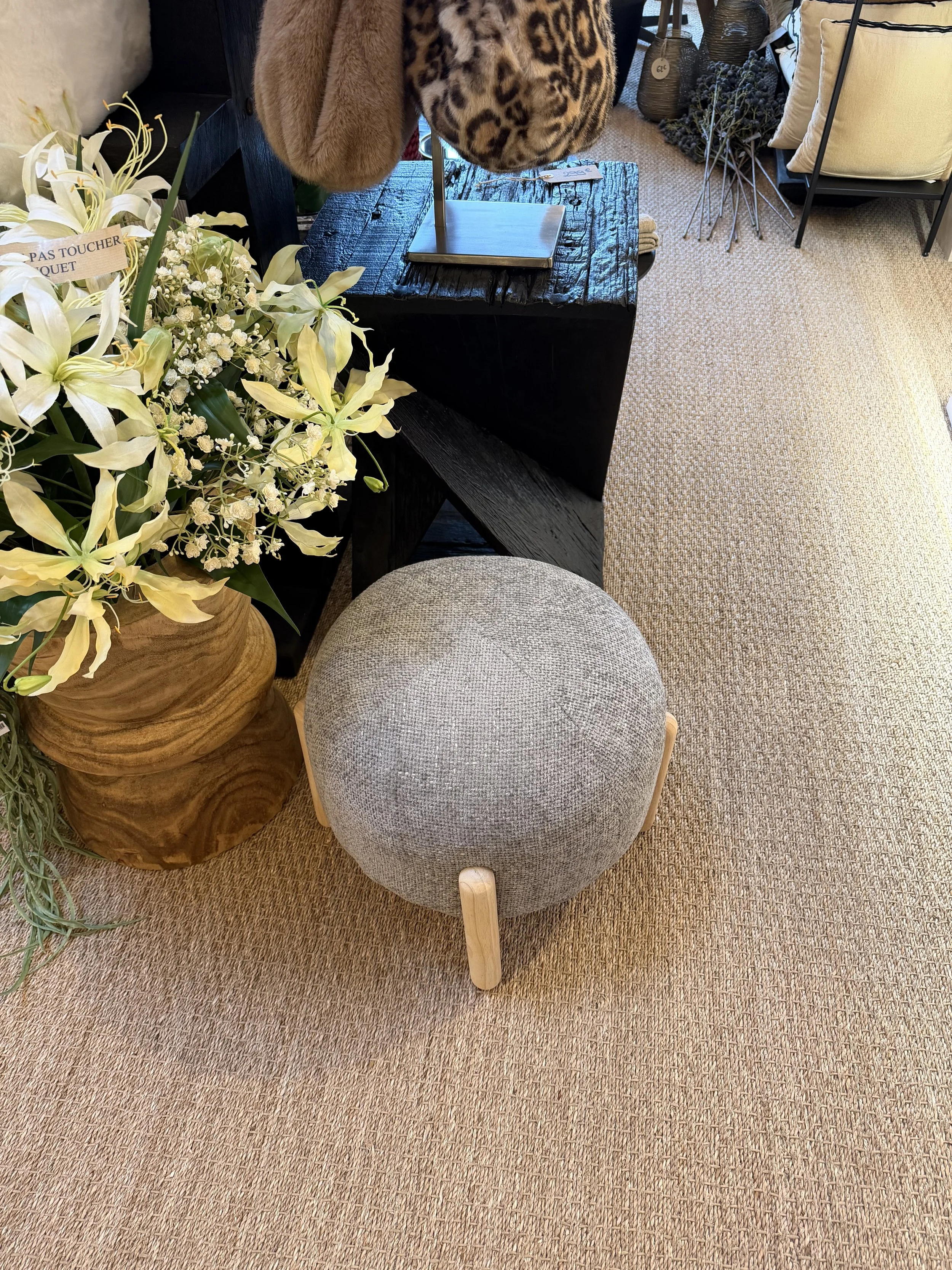 Pouf rond rembourré beige avec quatre pieds en bois clair, placé sur un tapis beige dans un intérieur décoratif.