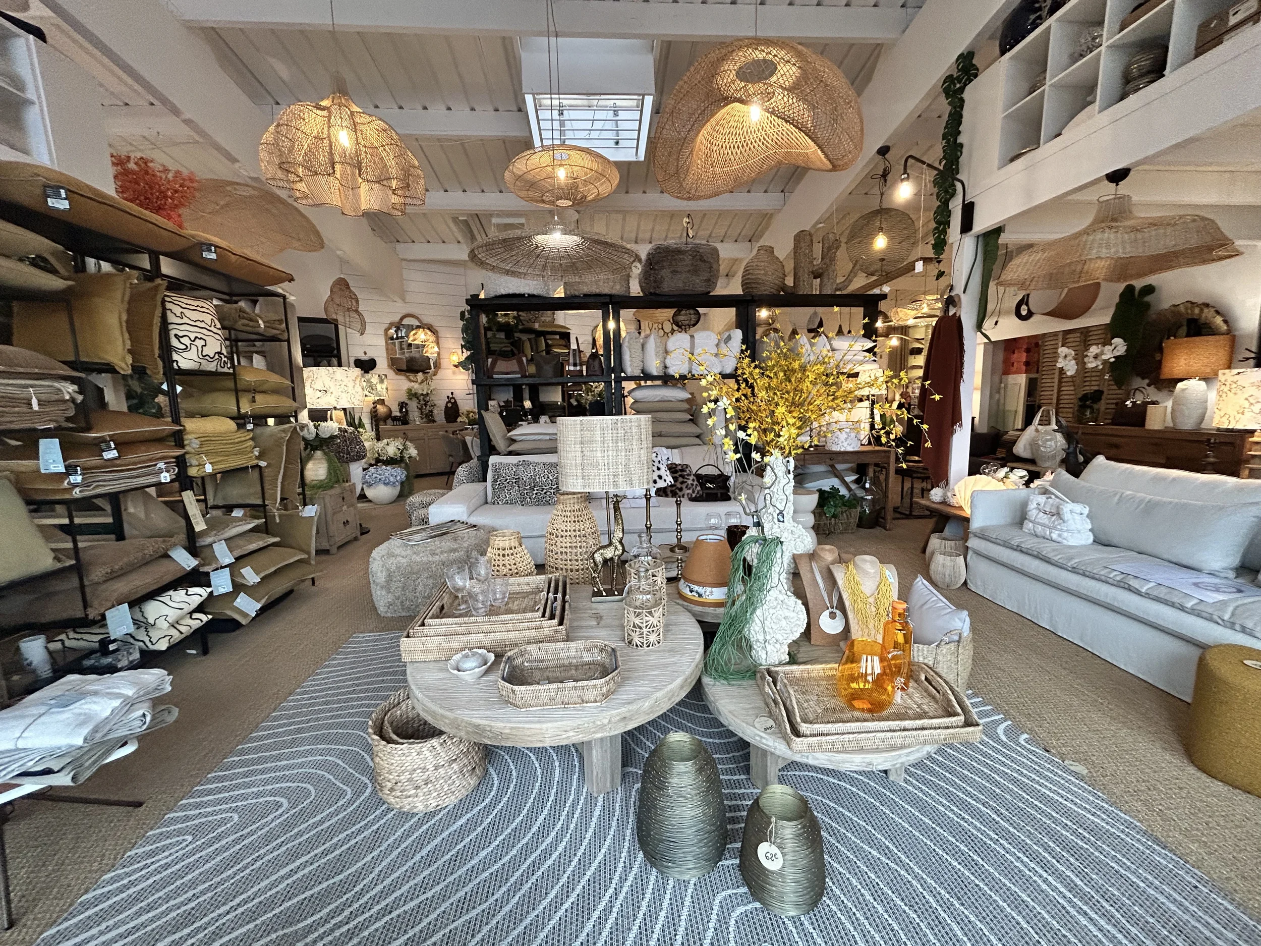 Intérieur d'un magasin de décoration avec canapé blanc, meubles en rotin, lampes en osier, et divers objets décoratifs en matériaux naturels.