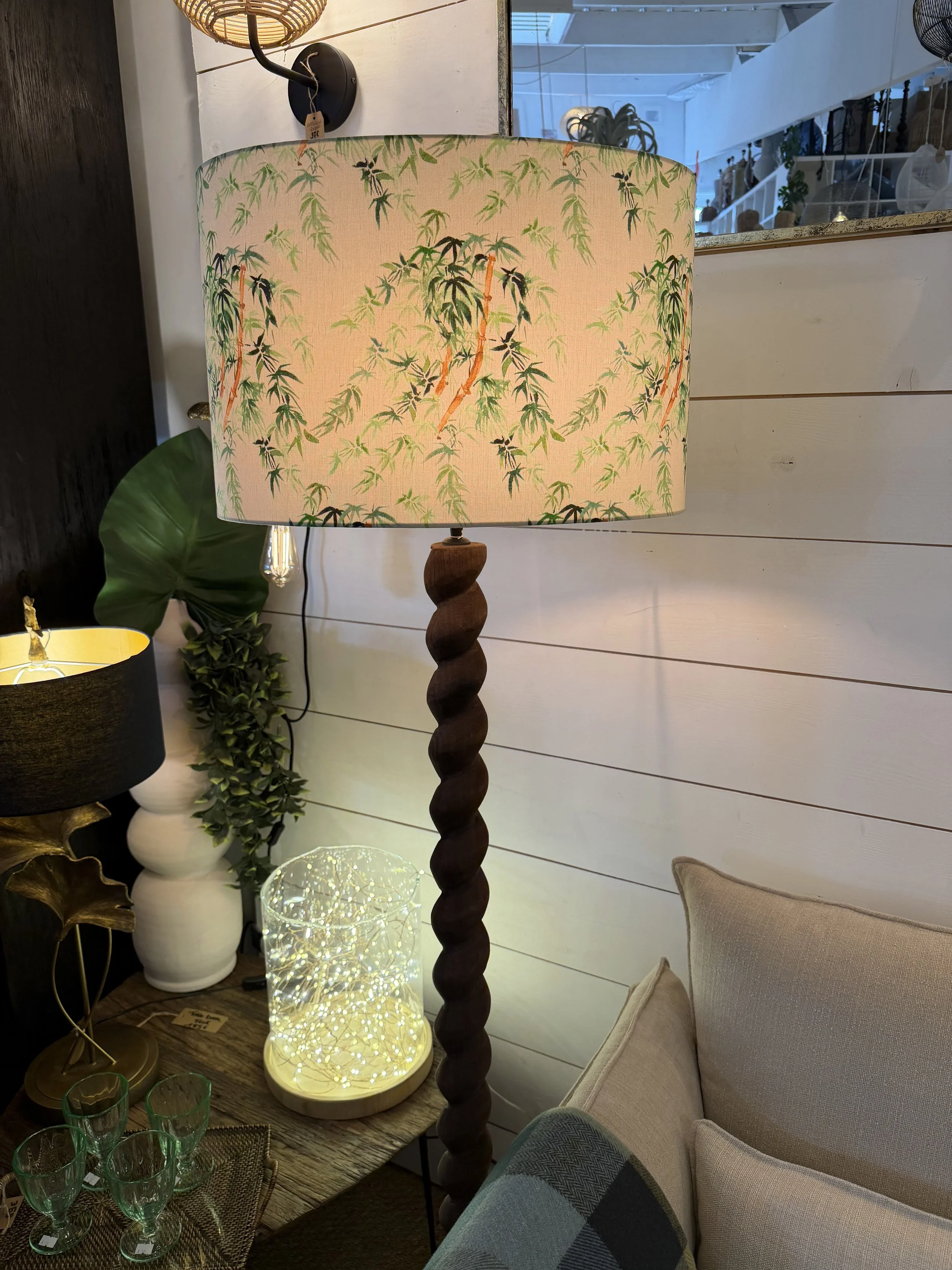 Lampe sur pied avec un abat-jour décoré de motifs de branches et feuilles vertes. Le pied de la lampe est en bois torsadé.