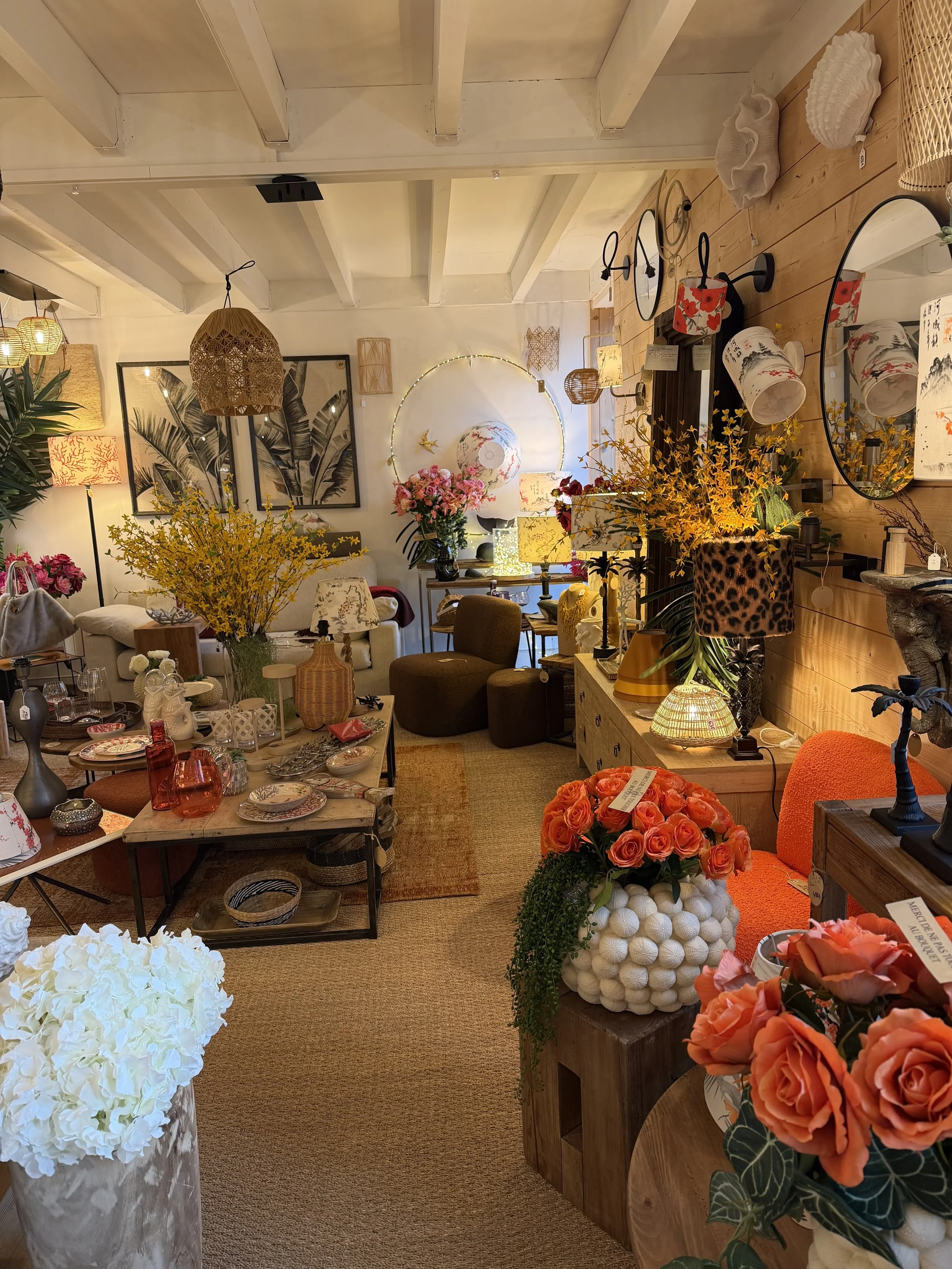 Intérieur d'une boutique de décoration avec des fleurs, lampes, miroirs, tableaux et meubles en bois.