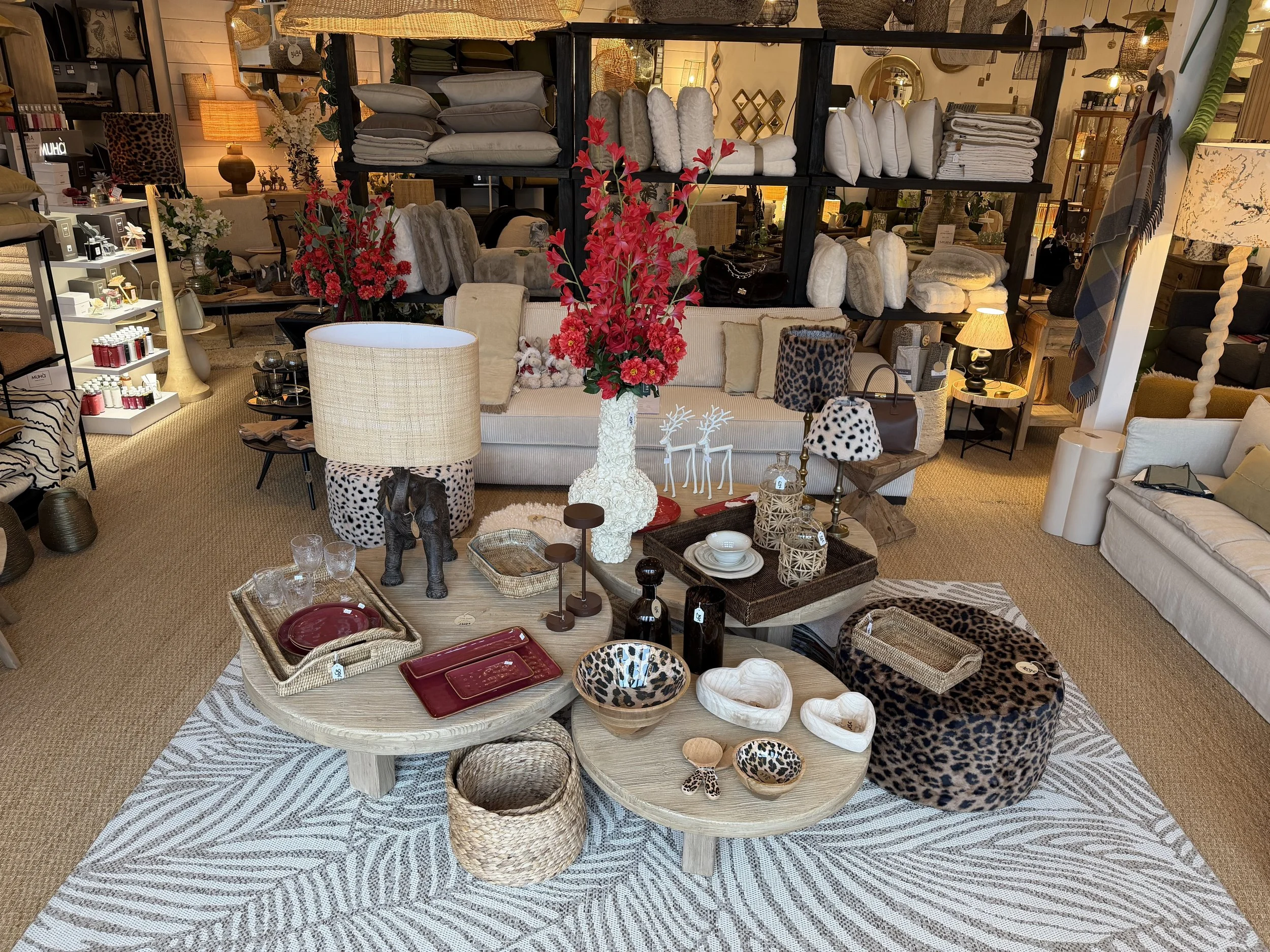 Intérieur d'un magasin de décoration avec plusieurs meubles, lampes, vases, vaisselle et accessoires, y compris un canapé beige, des étagères avec linge de maison, et une table basse avec des objets décoratifs