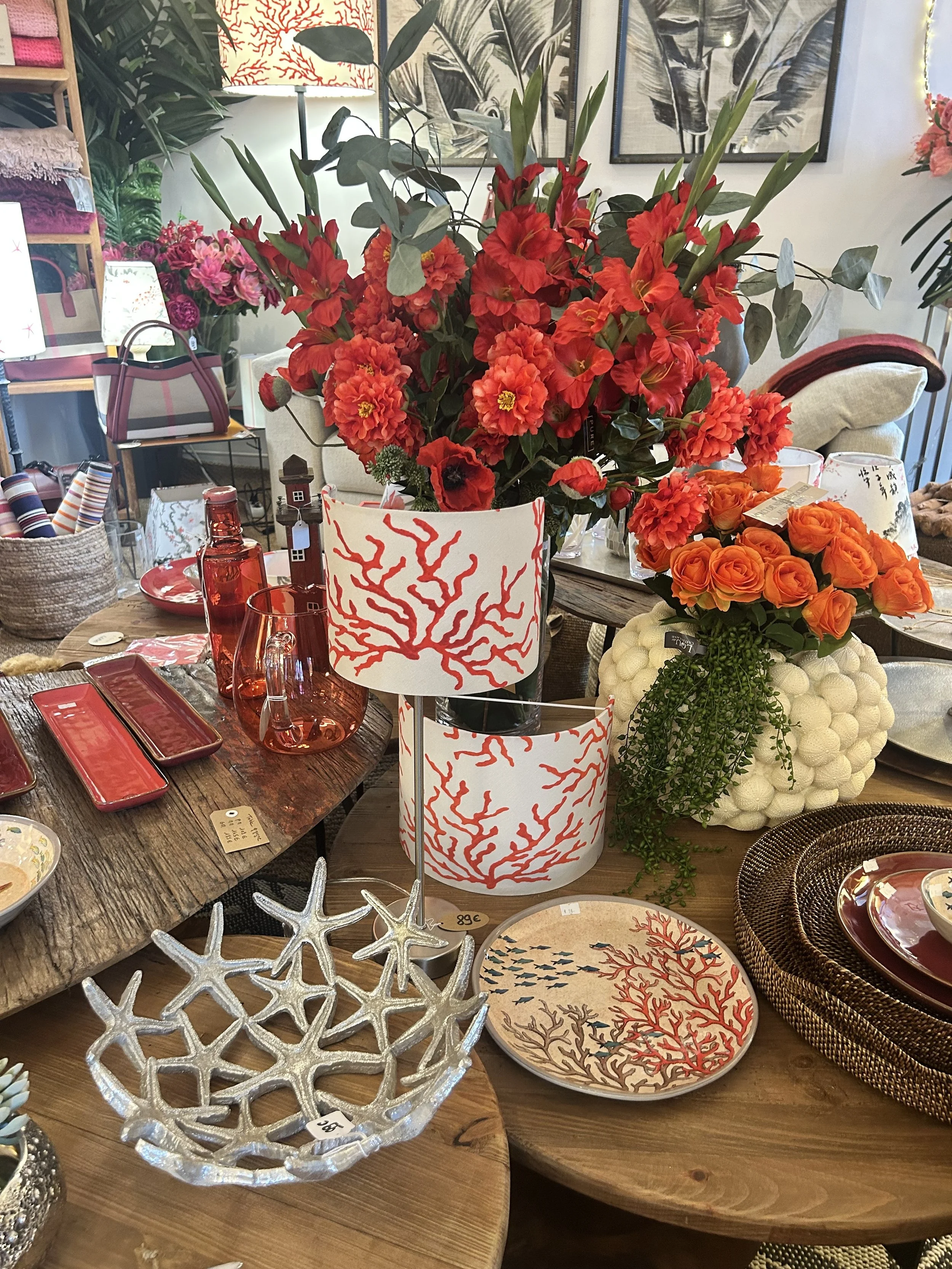 Vase avec un grand bouquet de fleurs rouges et orange, décorations en forme de corail rouge sur les vases, plats décoratifs avec des motifs de corail, et divers objets de décoration dans une boutique d'intérieur.
