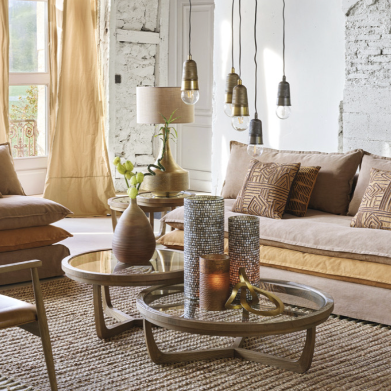 Salon moderne avec canapé beige, tables basses en bois, lampadaire et plusieurs pendentifs suspendus, décorations avec vases et bougies.