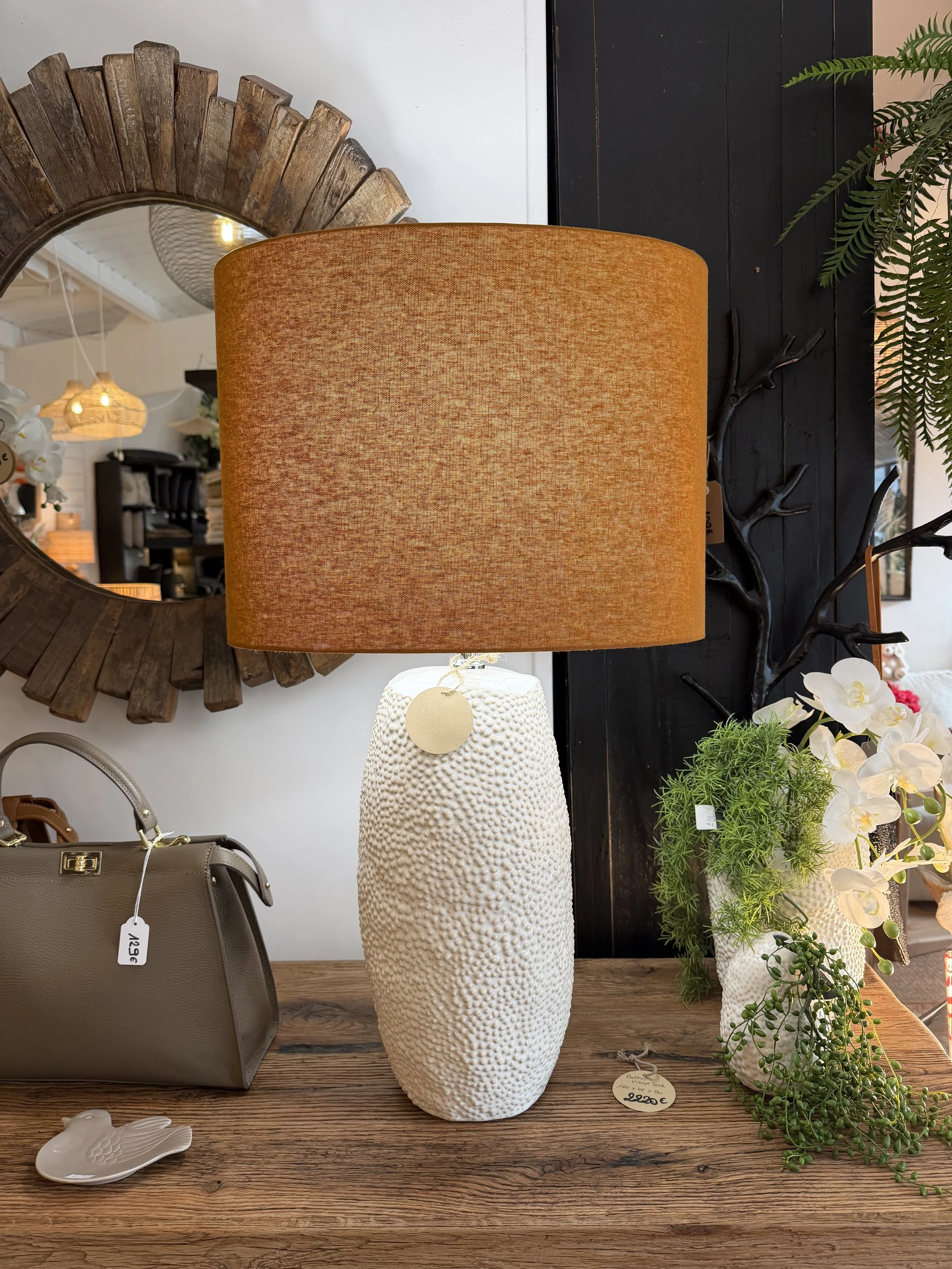 lampe de table avec un vase blanc texturé, entourée de plantes vertes et d'objets décoratifs, dans un magasin d'intérieur