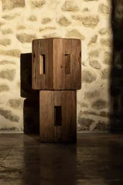 Deux blocs de bois debout, l'un sur l'autre, avec des formes rectangulaires taillées, en devant d'un mur en pierre.