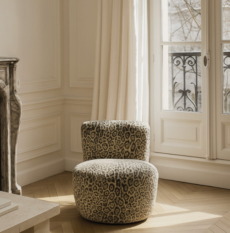 Fauteuil en tissu avec motif léopard dans une pièce lumineuse avec grande fenêtre et rideaux blancs.