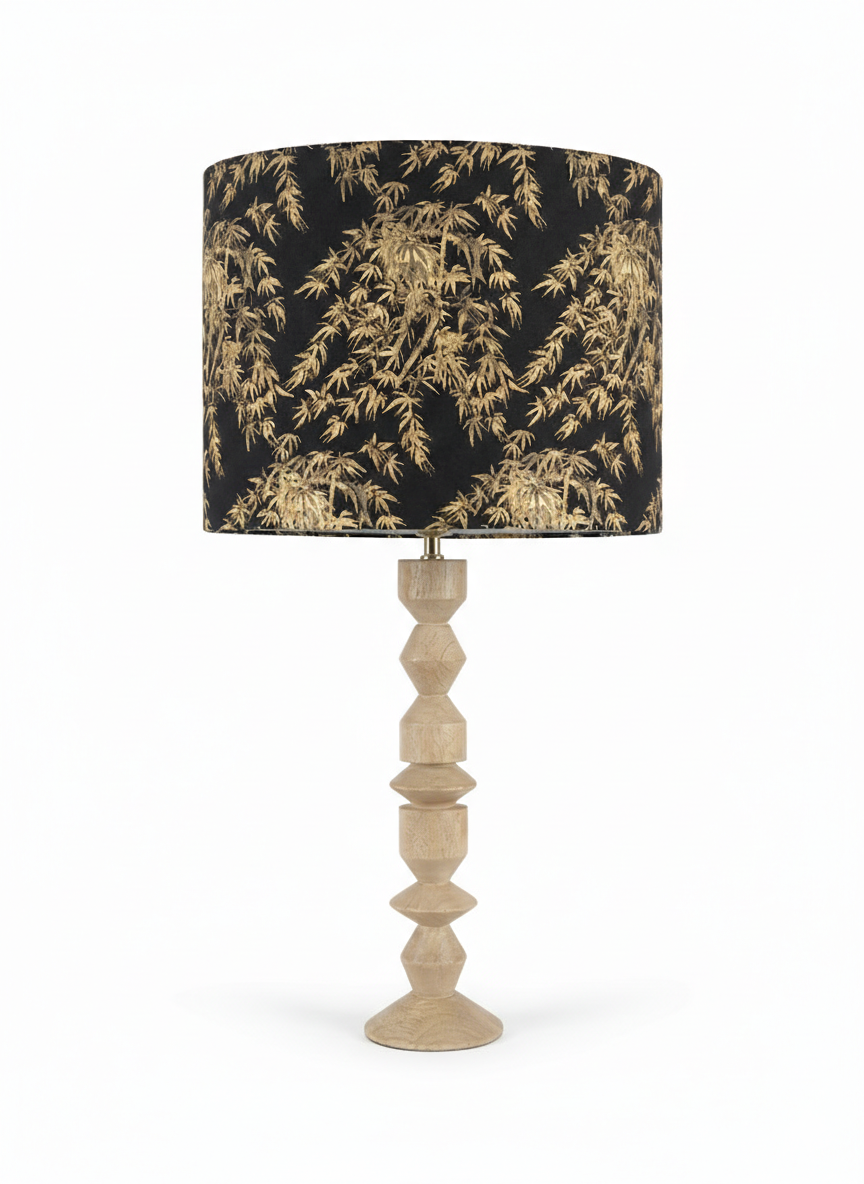 Lampe de table avec un abat-jour noir à motifs dorés de feuilles d'arbres et un pied en bois sculpté.