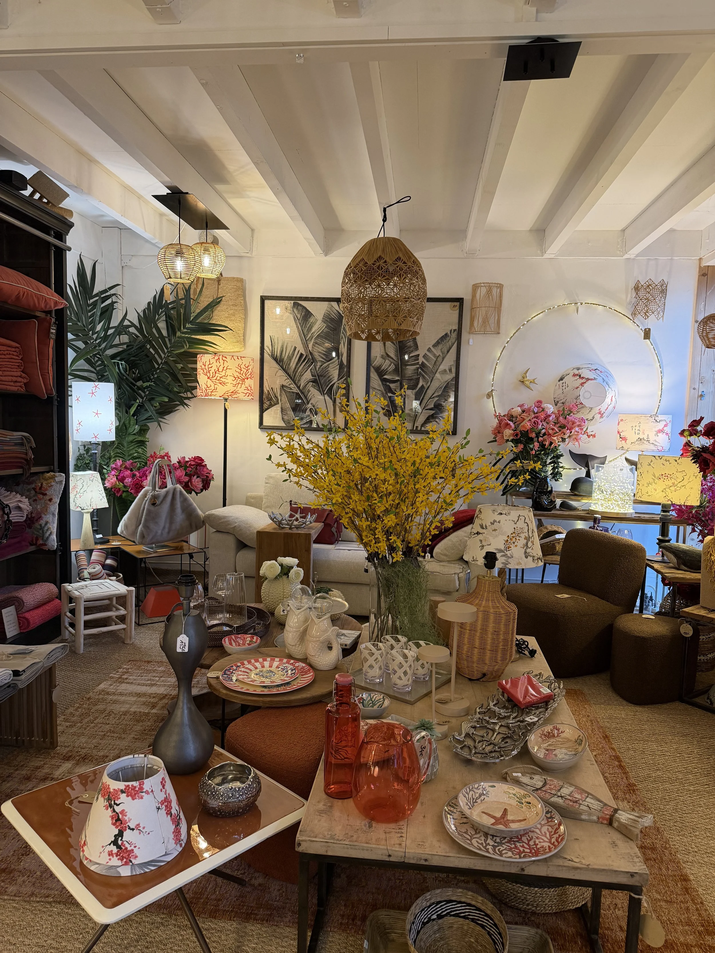 Une décoration intérieure avec un canapé beige, des fleurs colorées, des lampes, des objets en céramique, des vases en verre, des tableaux et des meubles en bois, créant une ambiance chaleureuse et éclectique.