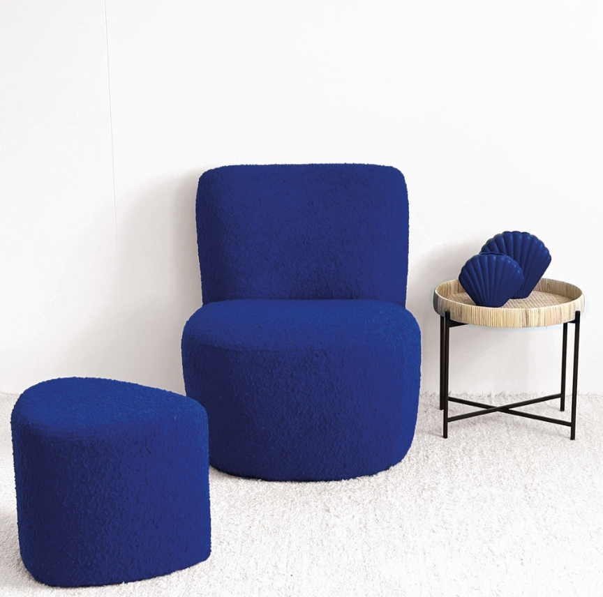 Deux sièges bleus en forme de pouf dans une pièce blanche, à côté d'une table ronde en bois avec deux objets décoratifs bleus en forme de coquillage.
