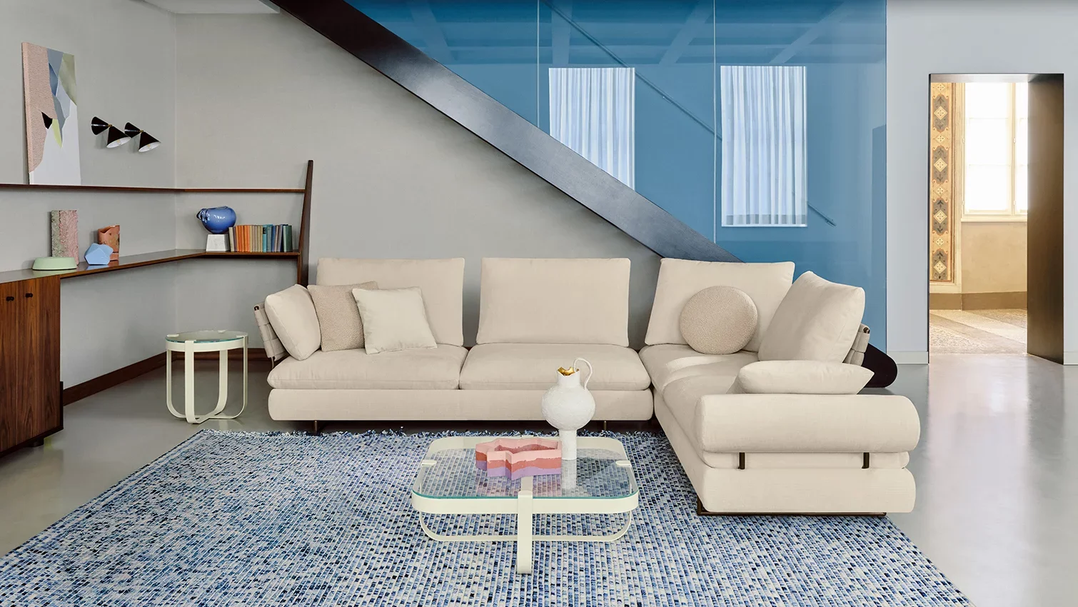 Salon moderne avec canapé blanc, tapis tissé bleu, table basse en verre et décoration colorée.