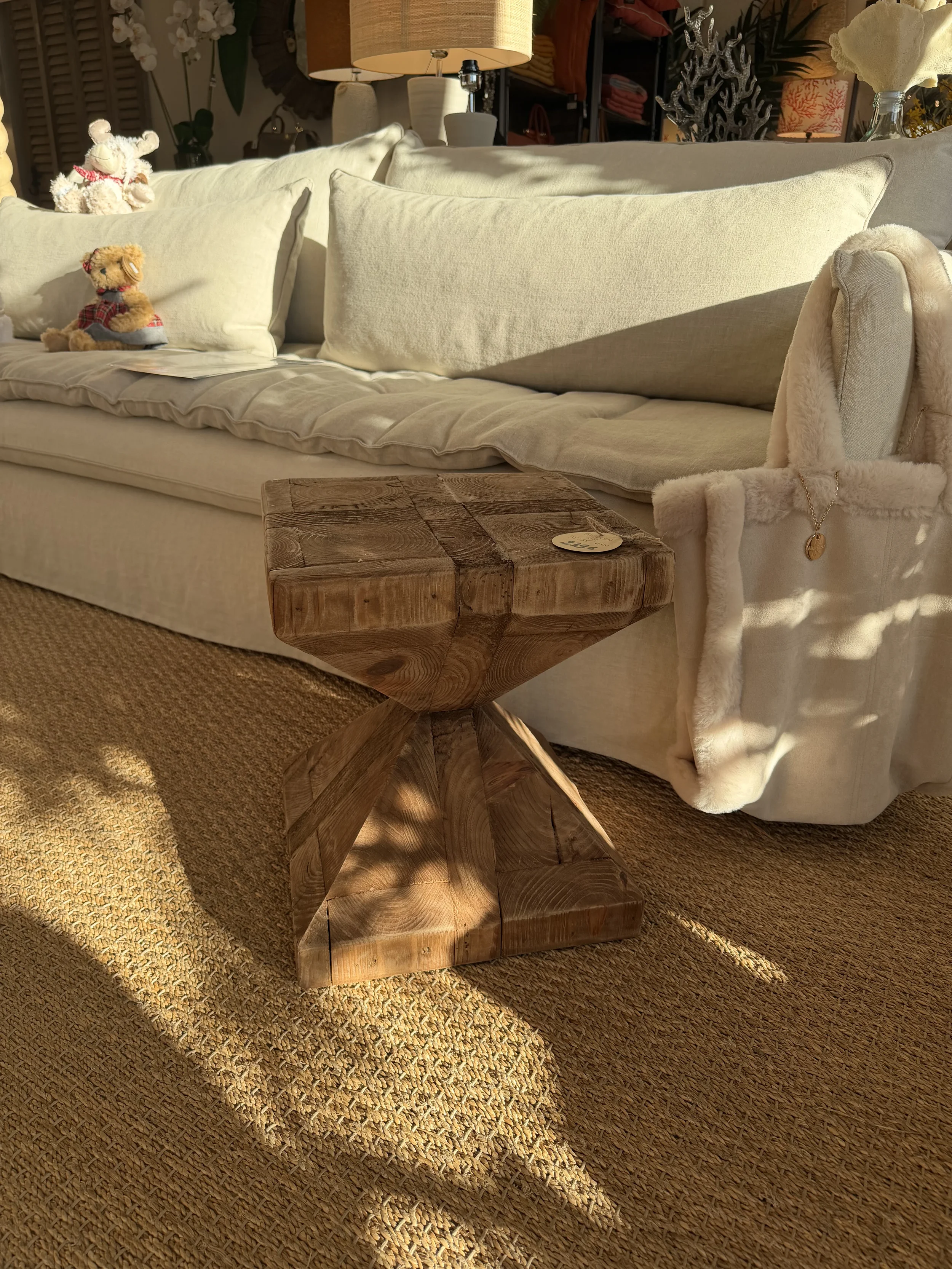 Table en bois rustique devant un canapé blanc avec des coussins, décorée dans une pièce chaleureuse.