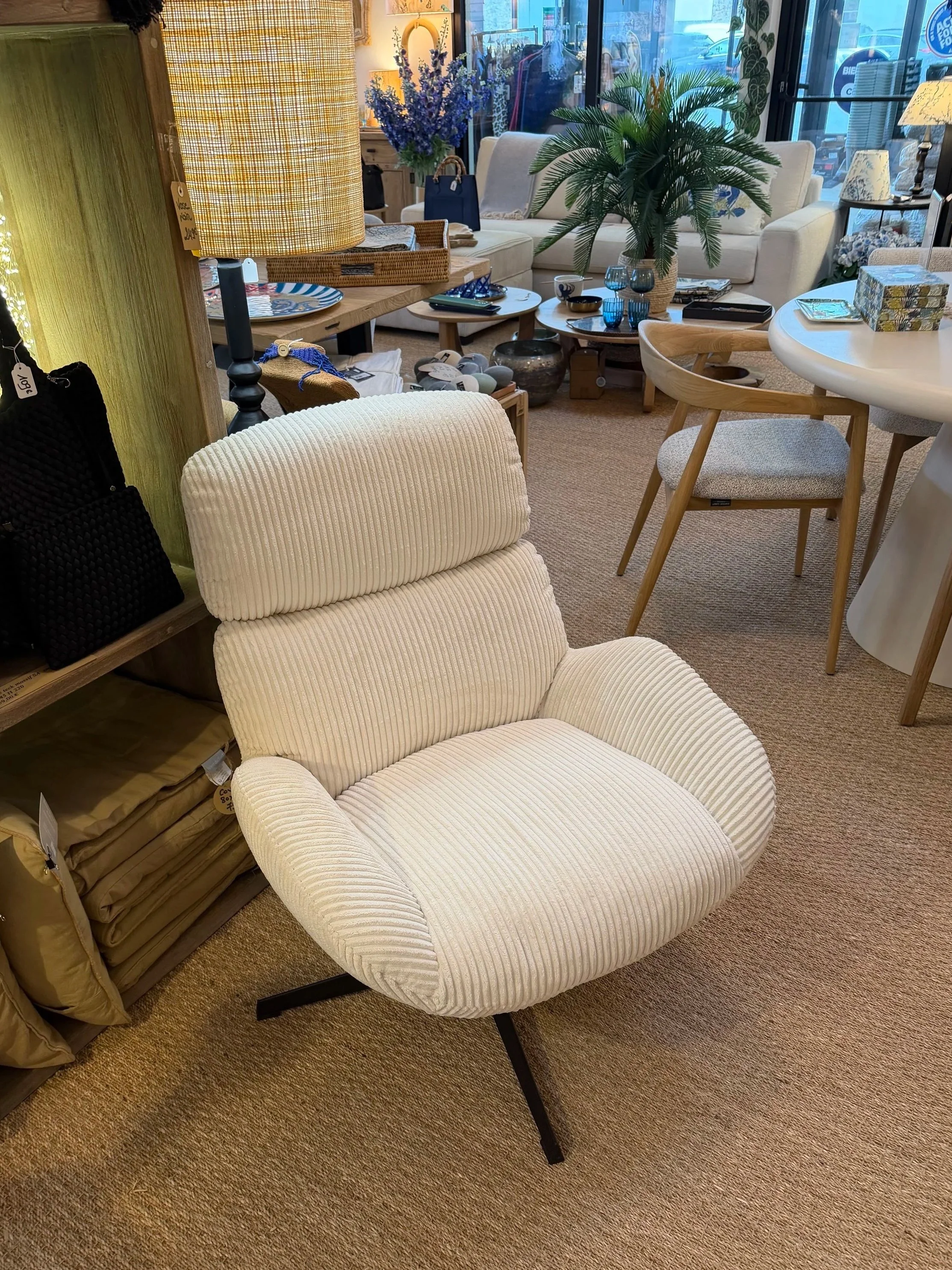 Fauteuil beige avec un dossier et des accoudoirs rembourrés en tissu rayé, placé dans un magasin de meubles