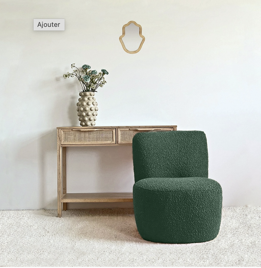 Une pièce avec une console en bois avec deux tiroirs en osier, une grande vase beige avec des fleurs séchées, un miroir en forme de cadre en bois, et un fauteuil vert foncé en tissu côtelé sur un tapis blanc.