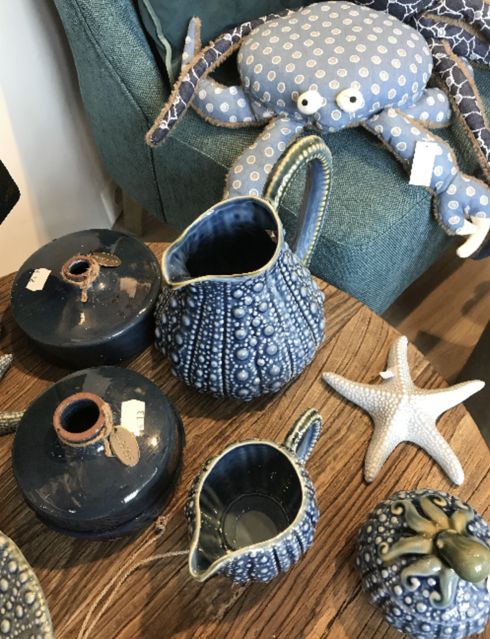 Objets décoratifs en céramique et porcelaine à thème marin, comprenant une étoile de mer, une carapace de tortue, des pots en céramique bleus et une pieuvre en tissu à pois sur un meuble en bois.