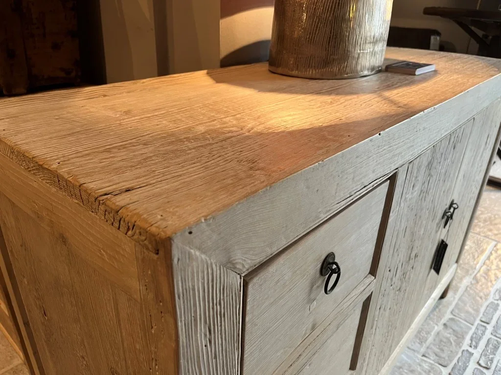 Un meuble en bois clair avec deux portes, un plateau en bois massif, une grande plante et un objet rectangulaire sur le dessus.