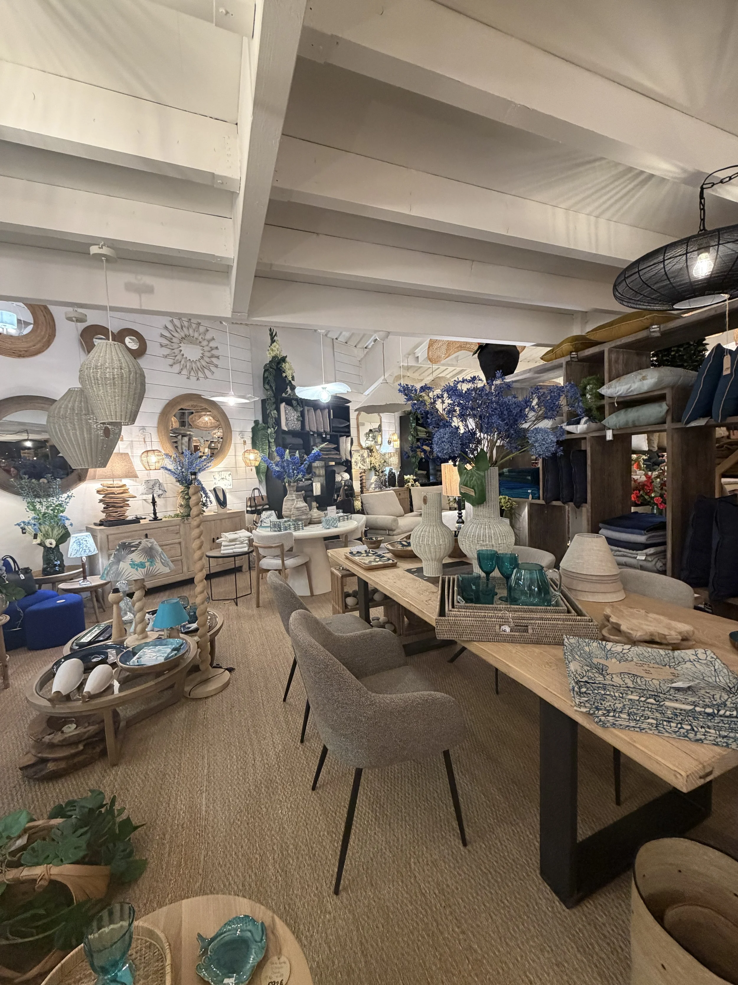 Intérieur d'une boutique de décoration avec des meubles, des vases, des lampes, des fleurs violettes et des objets décoratifs en bois.