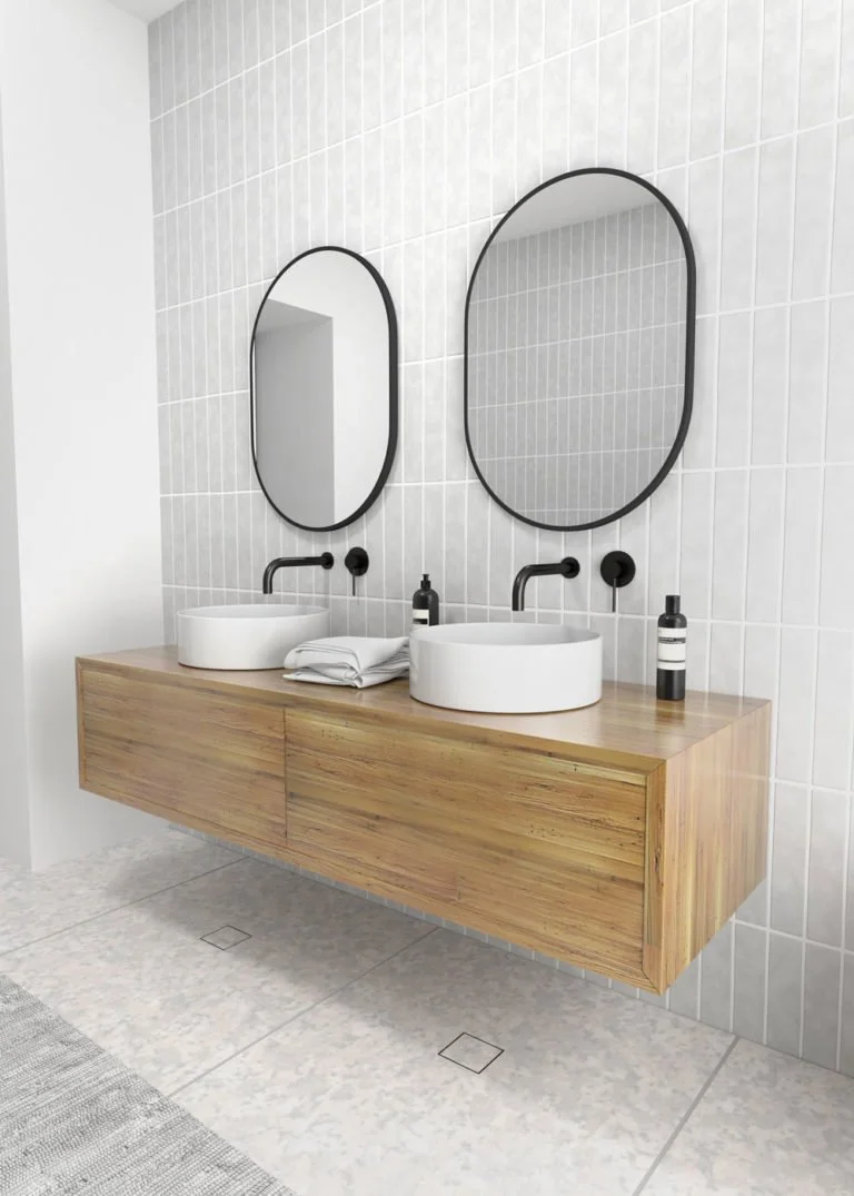 Modern bathroom with two oval mirrors, round white vessel sinks, black wall-mounted faucets, a wooden floating vanity, two black soap dispensers, and white tiles on the wall.