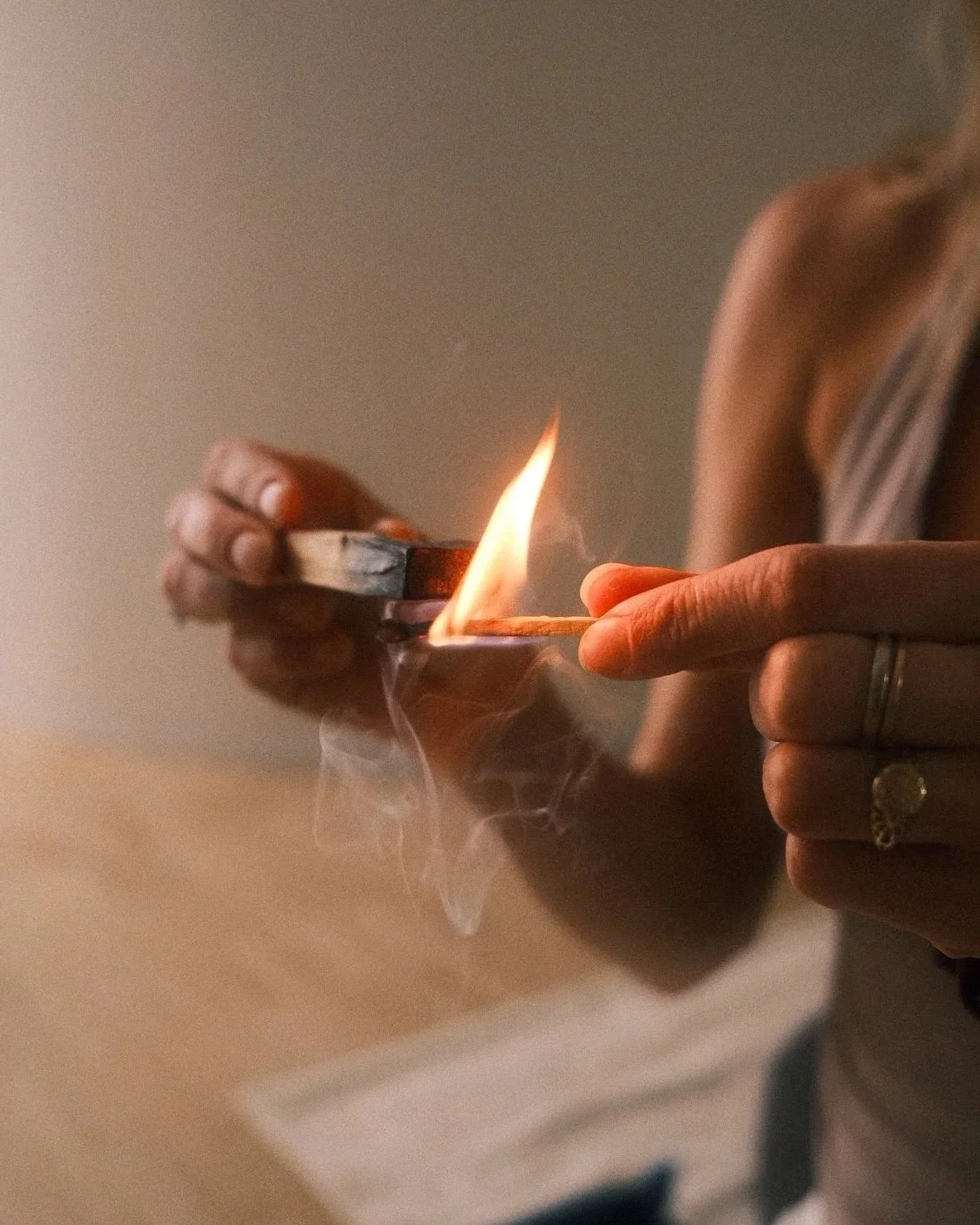 Person holding a matchstick near a small open flame, with a neutral beige background.