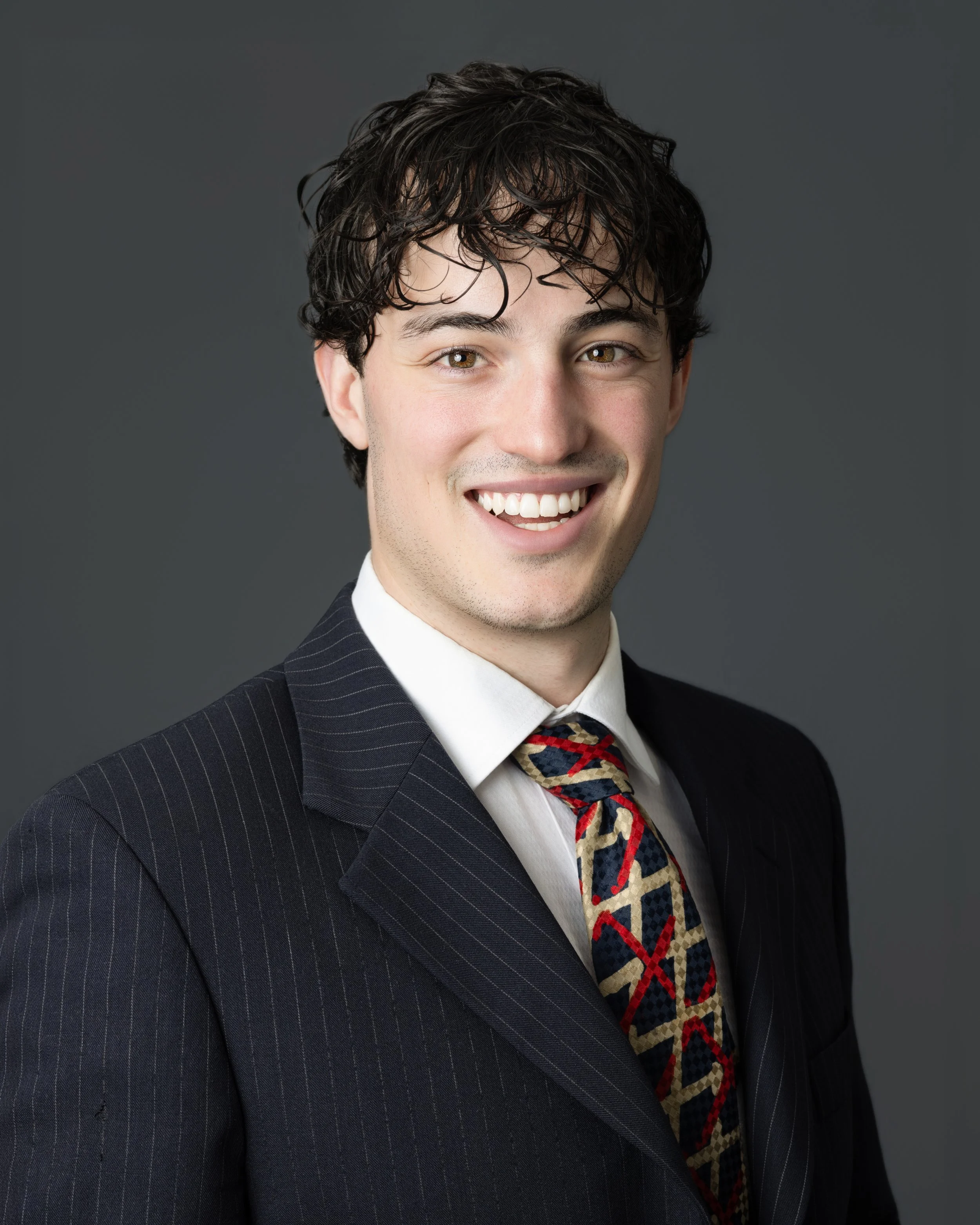 Black and white portrait of a young man with curly hair, wearing a suit and tie, smiling, facing slightly to the right, with a plain background.