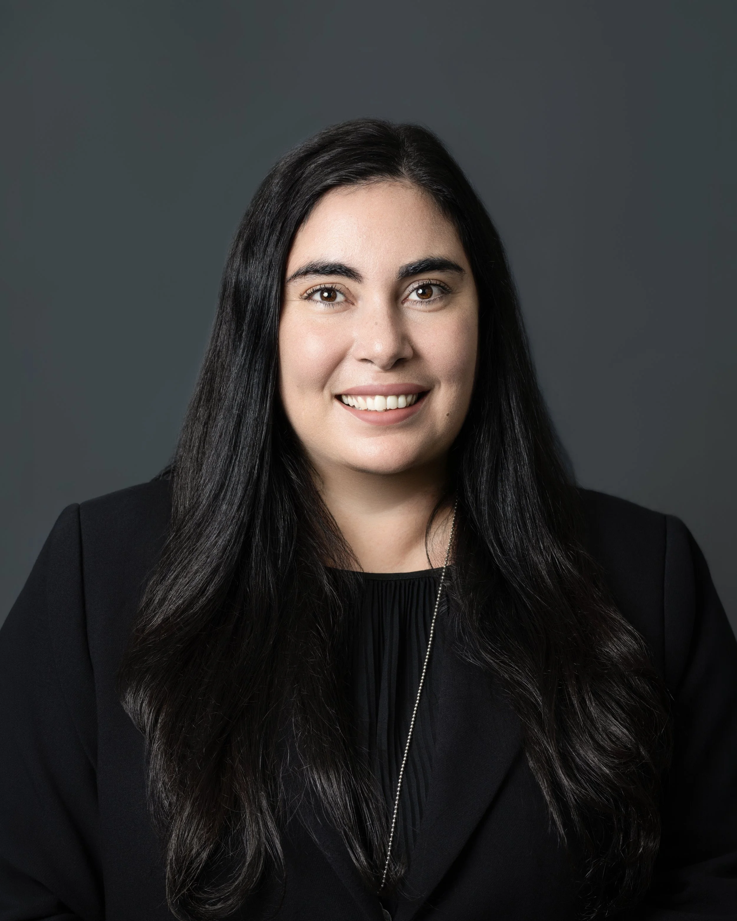 Black and white portrait of a smiling woman with long dark hair, wearing a dark top and necklace.