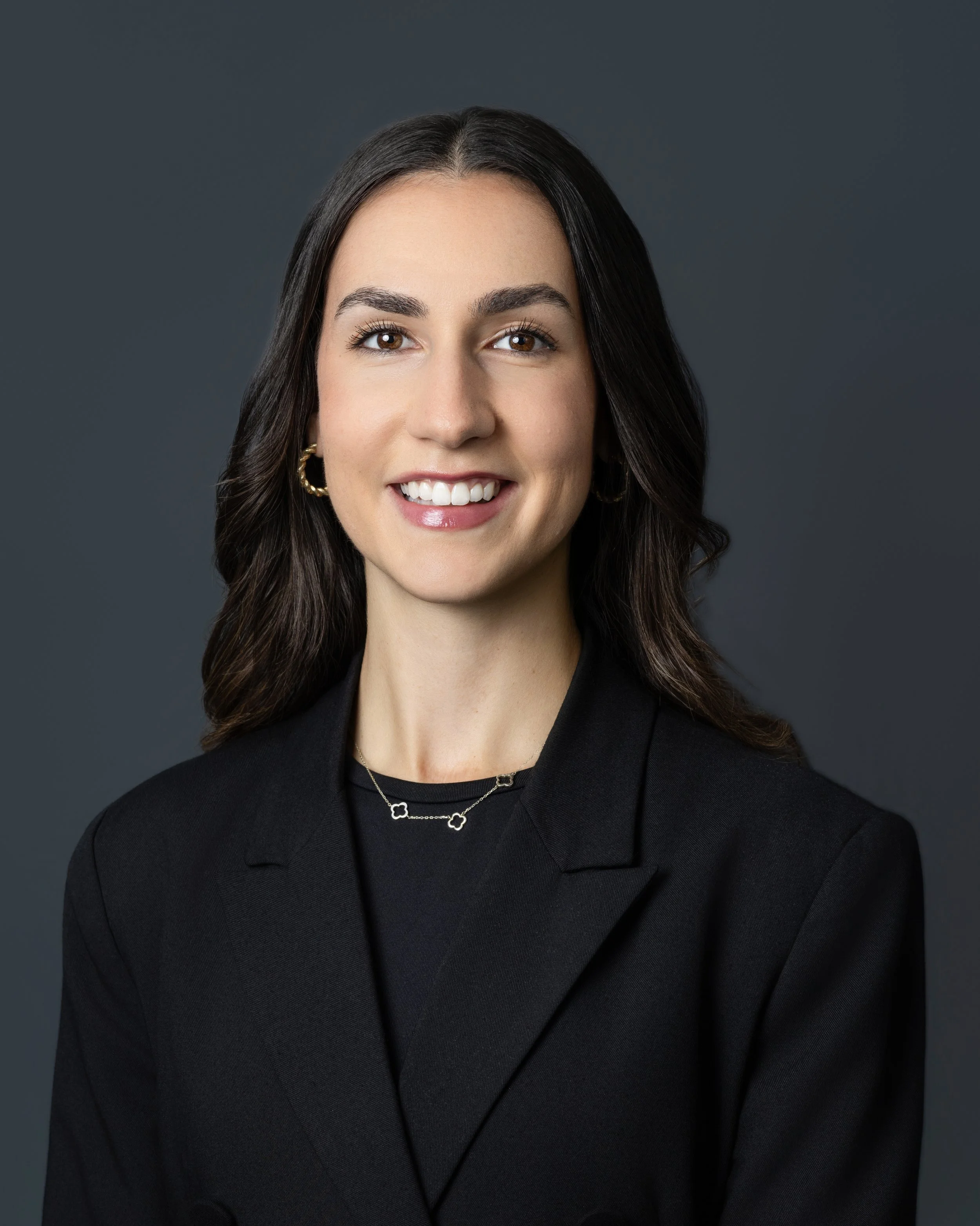 Black and white portrait of a smiling woman with shoulder-length hair, wearing a checkered blazer, a black top, and a necklace, in an indoor setting.