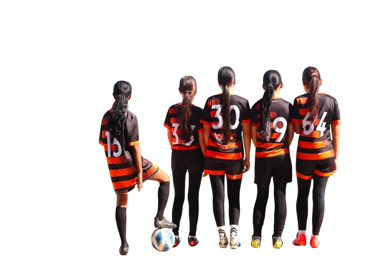 A group of five female soccer players in black and orange uniforms standing in a line with their backs to the camera, one player in the uniform holder with her foot on a soccer ball.