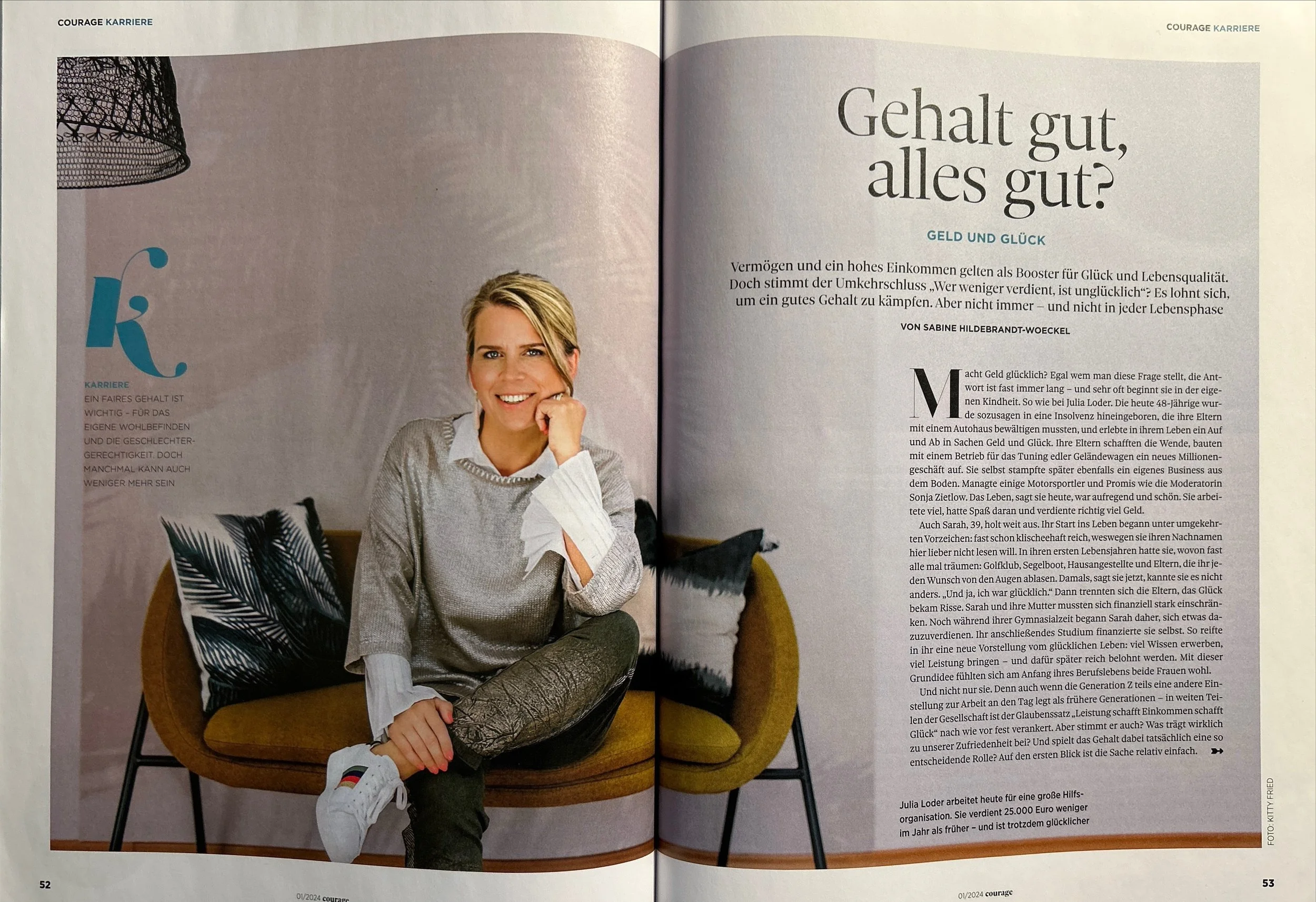 Ein offener Zeitschriftenartikel mit einem Portraitfoto einer lächelnden jungen Frau mit blondem Haar, sitzend auf einem Stuhl, vor einem hellen Hintergrund, modisch gekleidet in einem Grauen Pullover und einer weißen Bluse. Der Text des Artikels behandelt das Thema Geld und Glück.