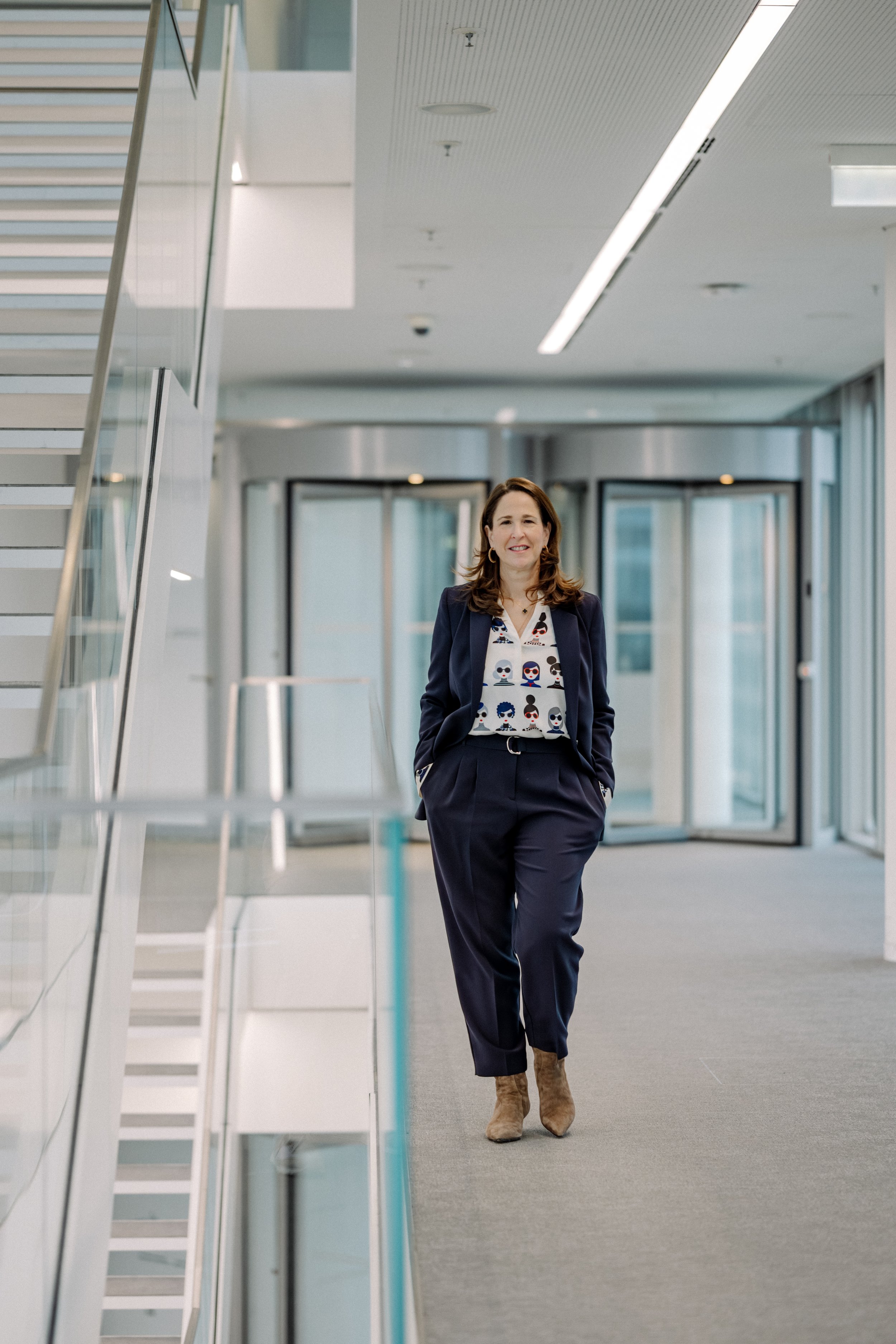 Eine junge Frau in Businesskleidung, die lächelnd durch ein modernes Bürogebäude geht.