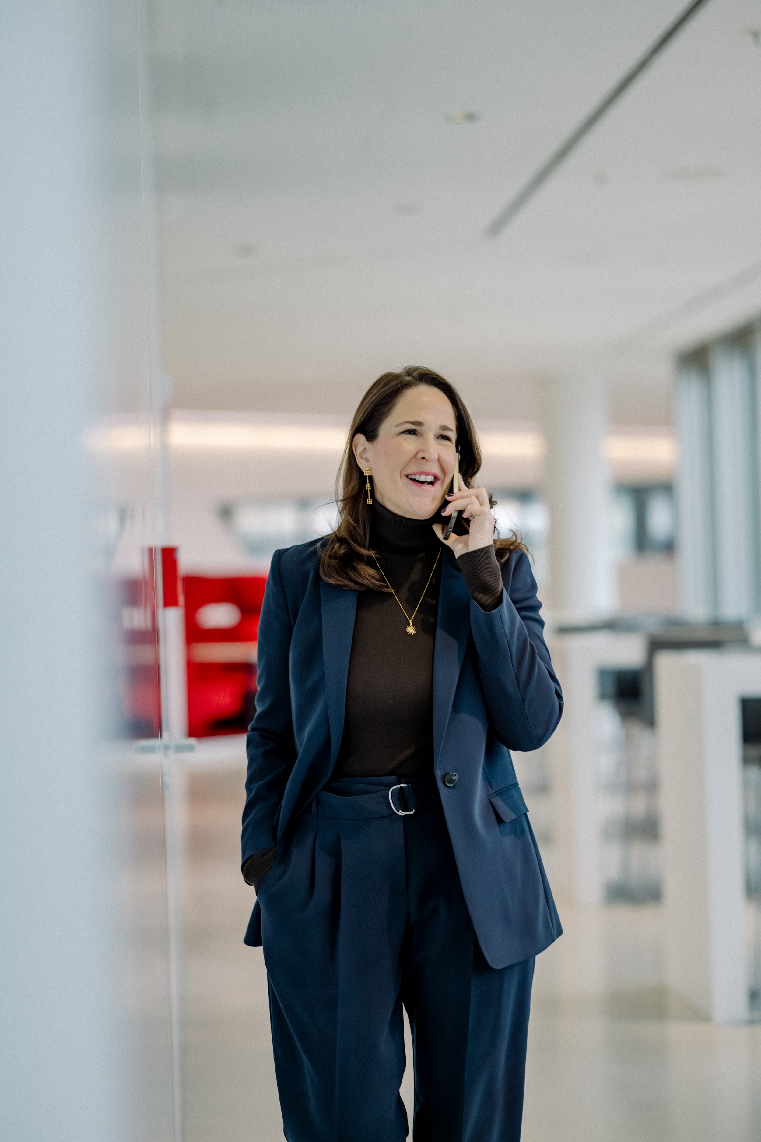 Eine lachende Frau spricht am Telefon in einem modernen Büroraum.