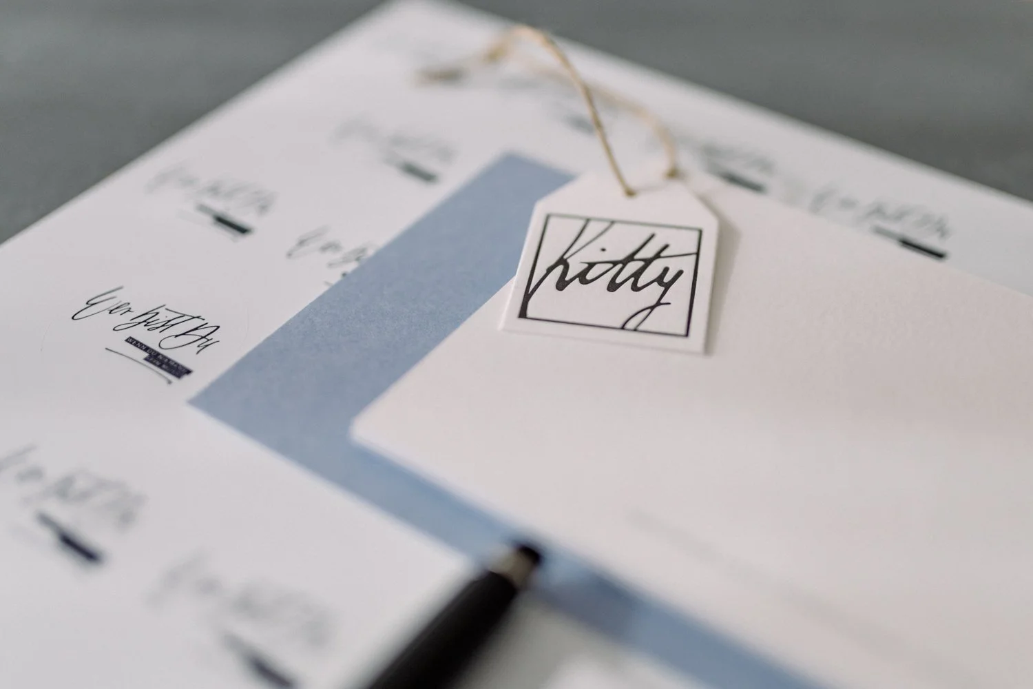 Aufkleber und Karten in Taubenblau, daran befestigt ein Namensschild in Letterpress mit "Kitty" Schriftzug