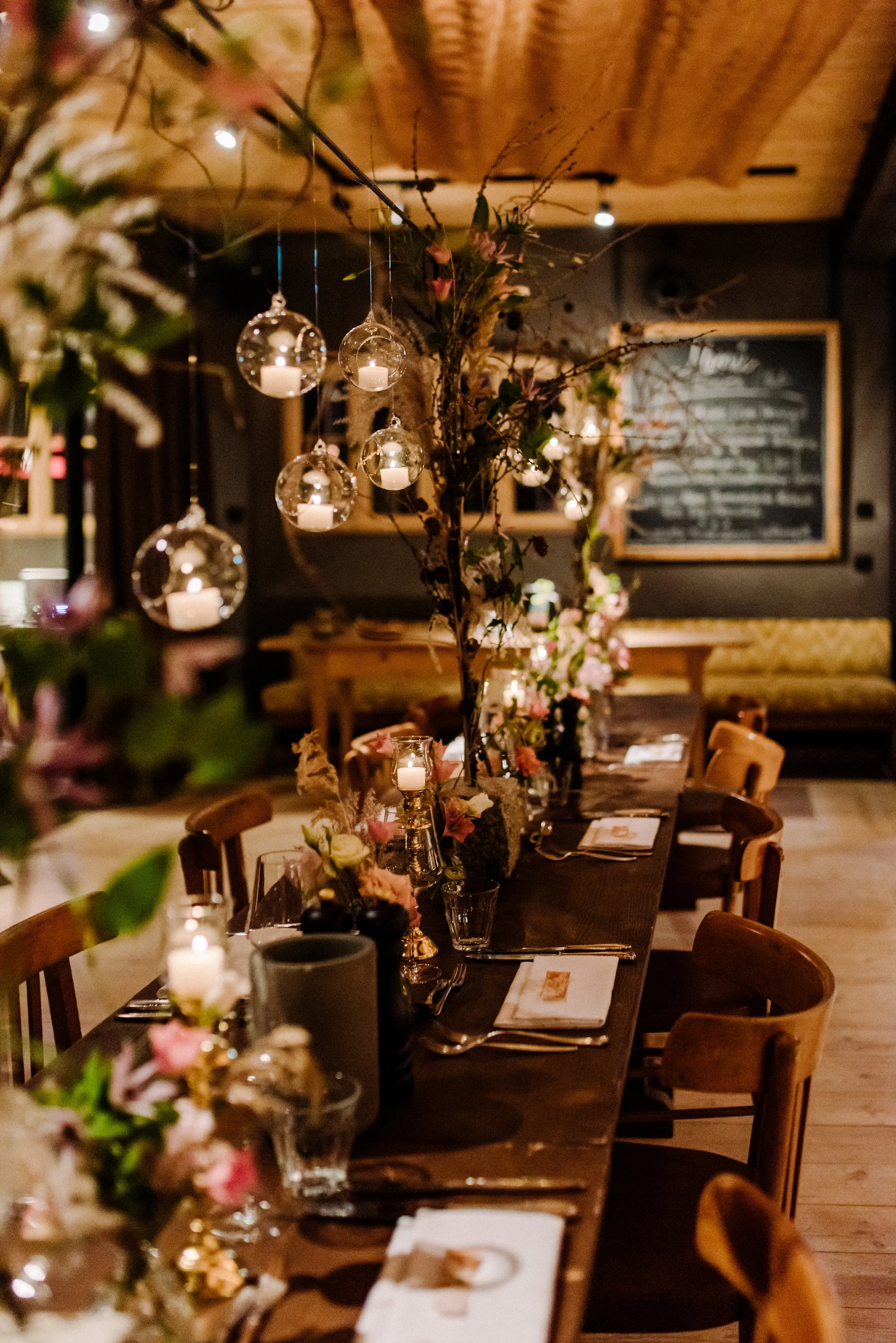 Ein langer Esstisch in einem rustikalen Restaurant, festlich dekoriert mit Blumen und Kerzen, mit Stühlen an beiden Seiten.